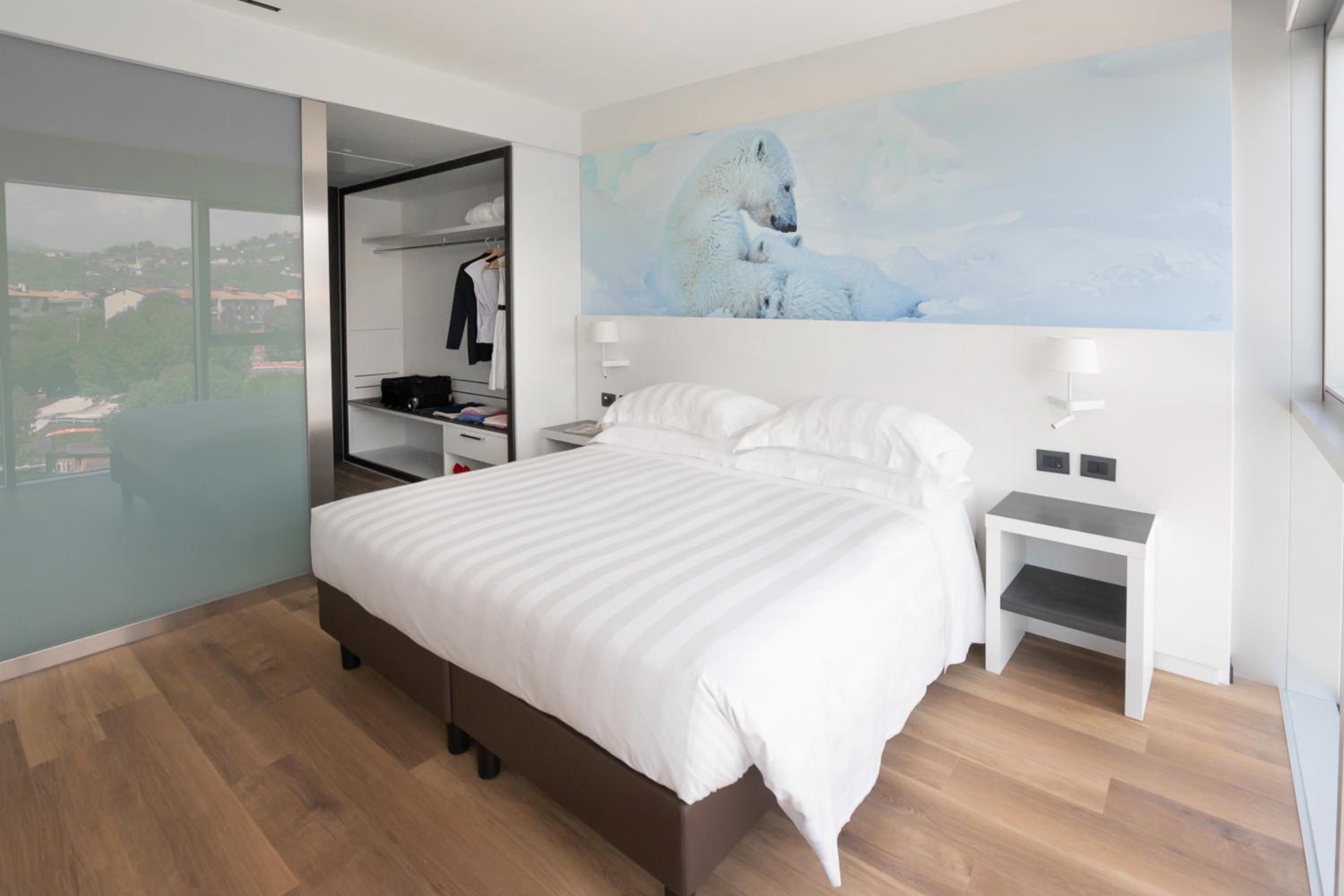A hotel bedroom with wood flooring, white linens, and a polar bear mural above the headboard.