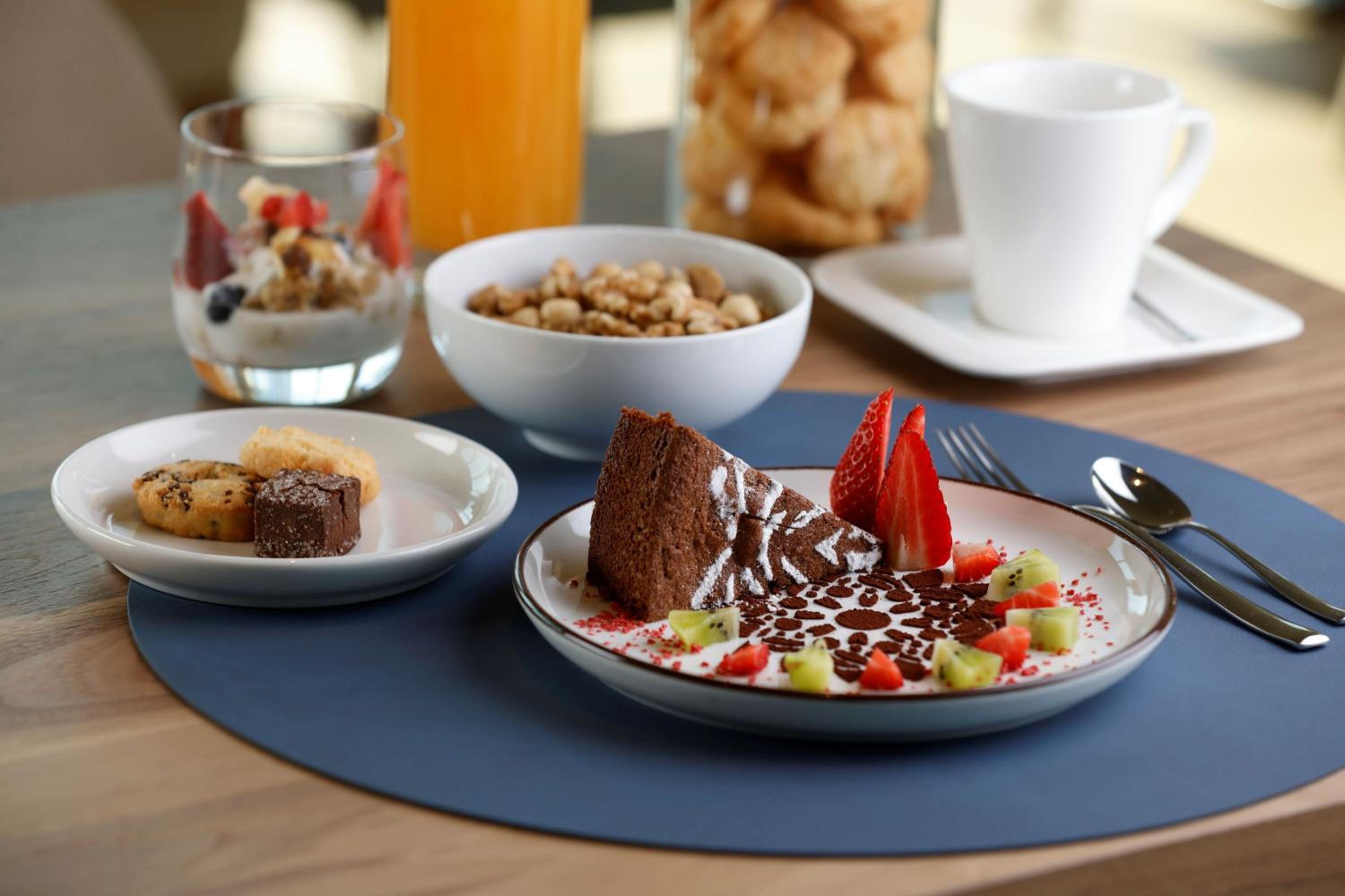 A table setting with chocolate cake garnished with fruit alongside breakfast cereal, cookies, and coffee.
