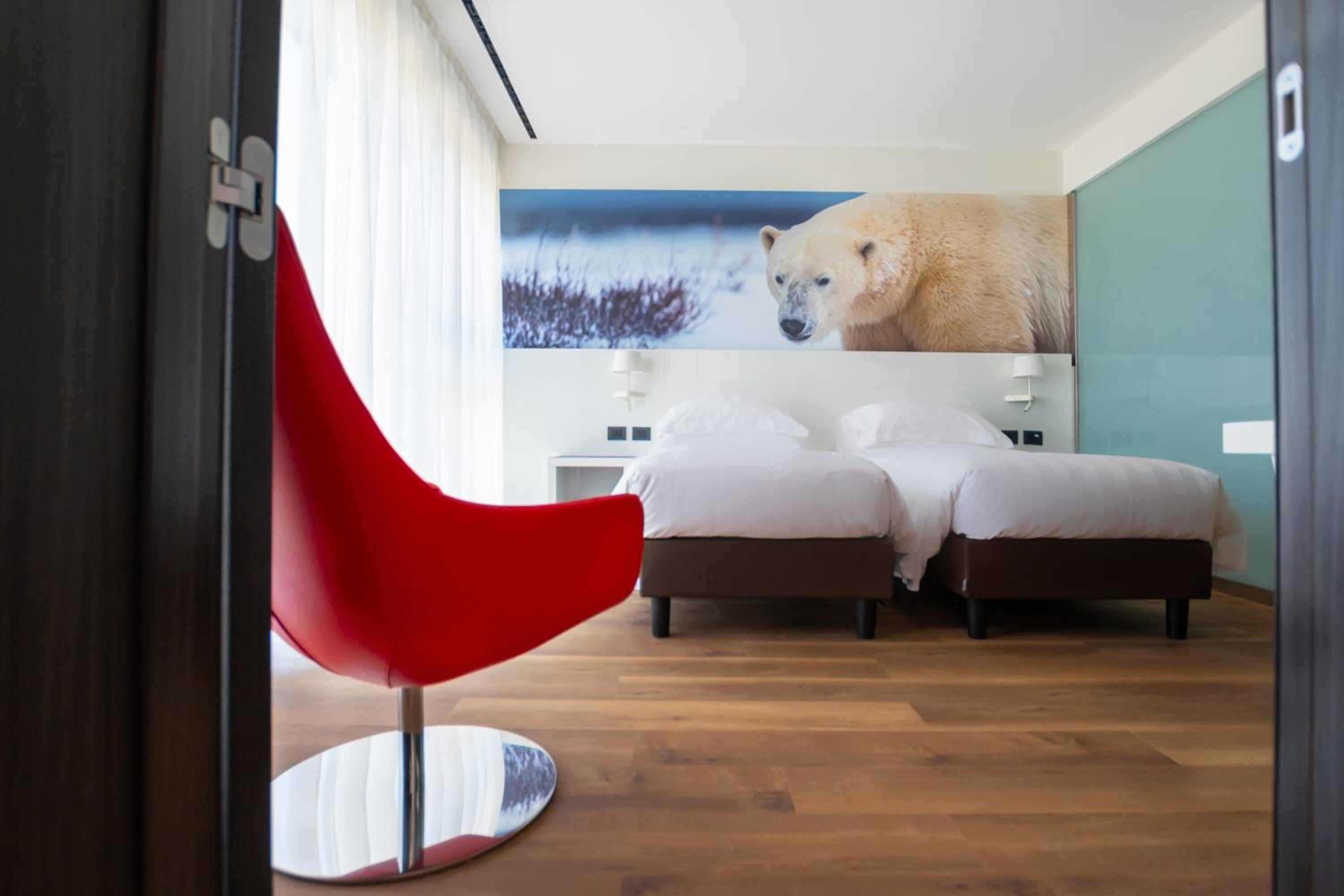 A bedroom viewed from a doorway, featuring beds beneath a polar bear wall print and a curved red chair.
