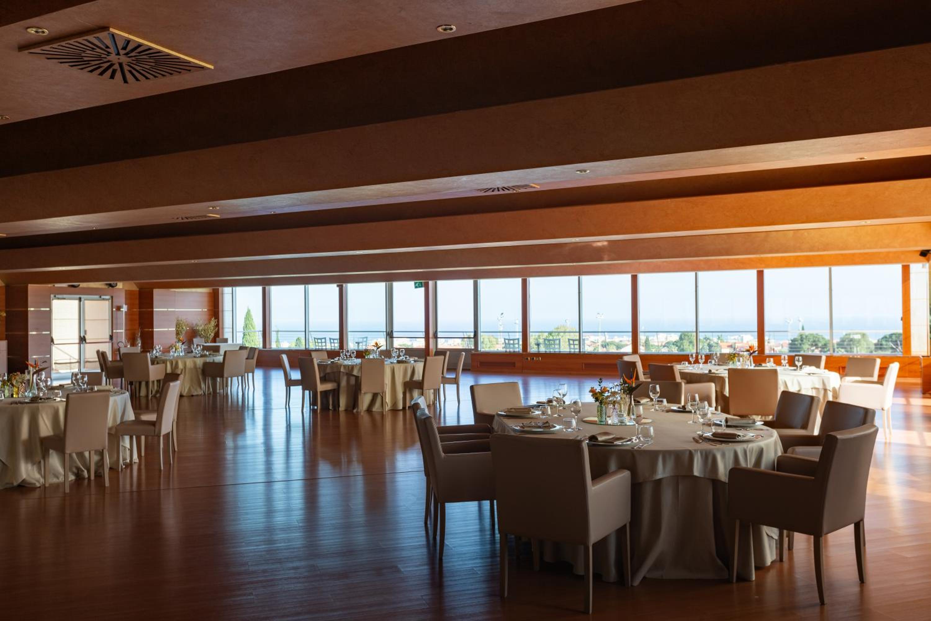 A spacious dining room features round set tables and wide panoramic windows overlooking the distant coast.