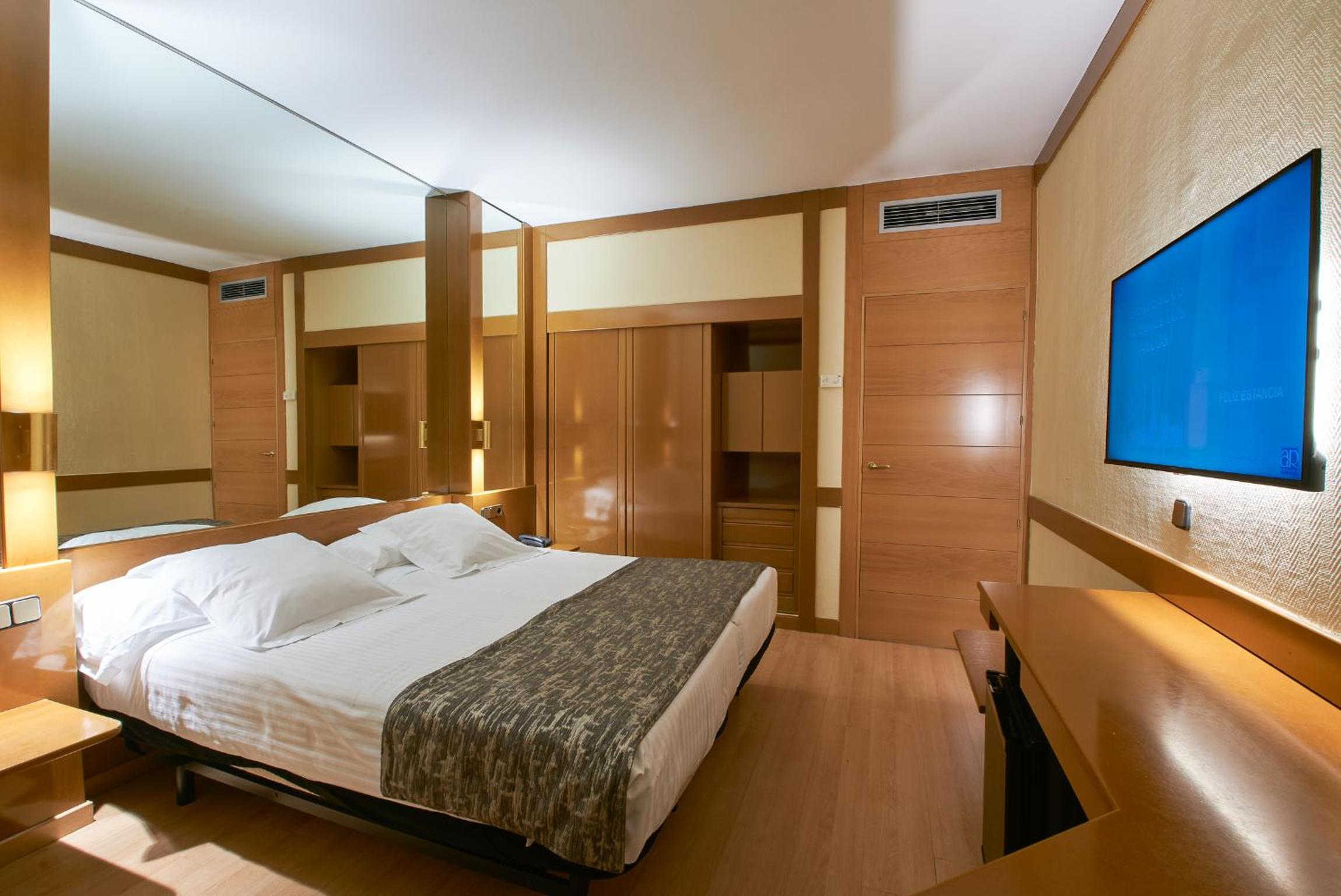 Hotel room featuring a made bed, wood wardrobe cabinetry, a mirrored accent wall, and a wall-mounted screen.