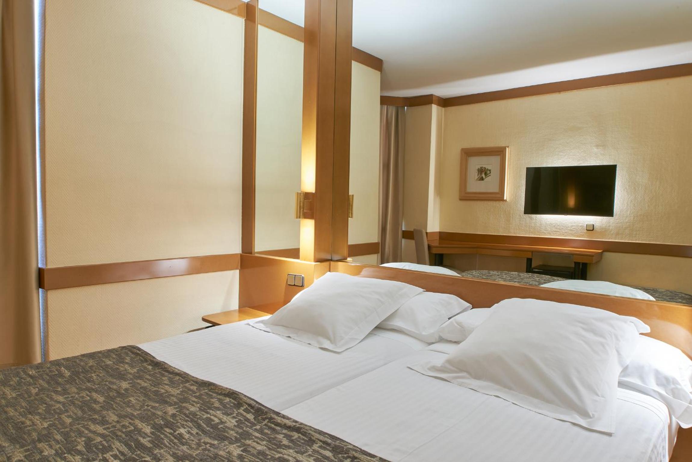 Bed with white pillows and patterned runner set against a wood-paneled wall with large mirrored sections.