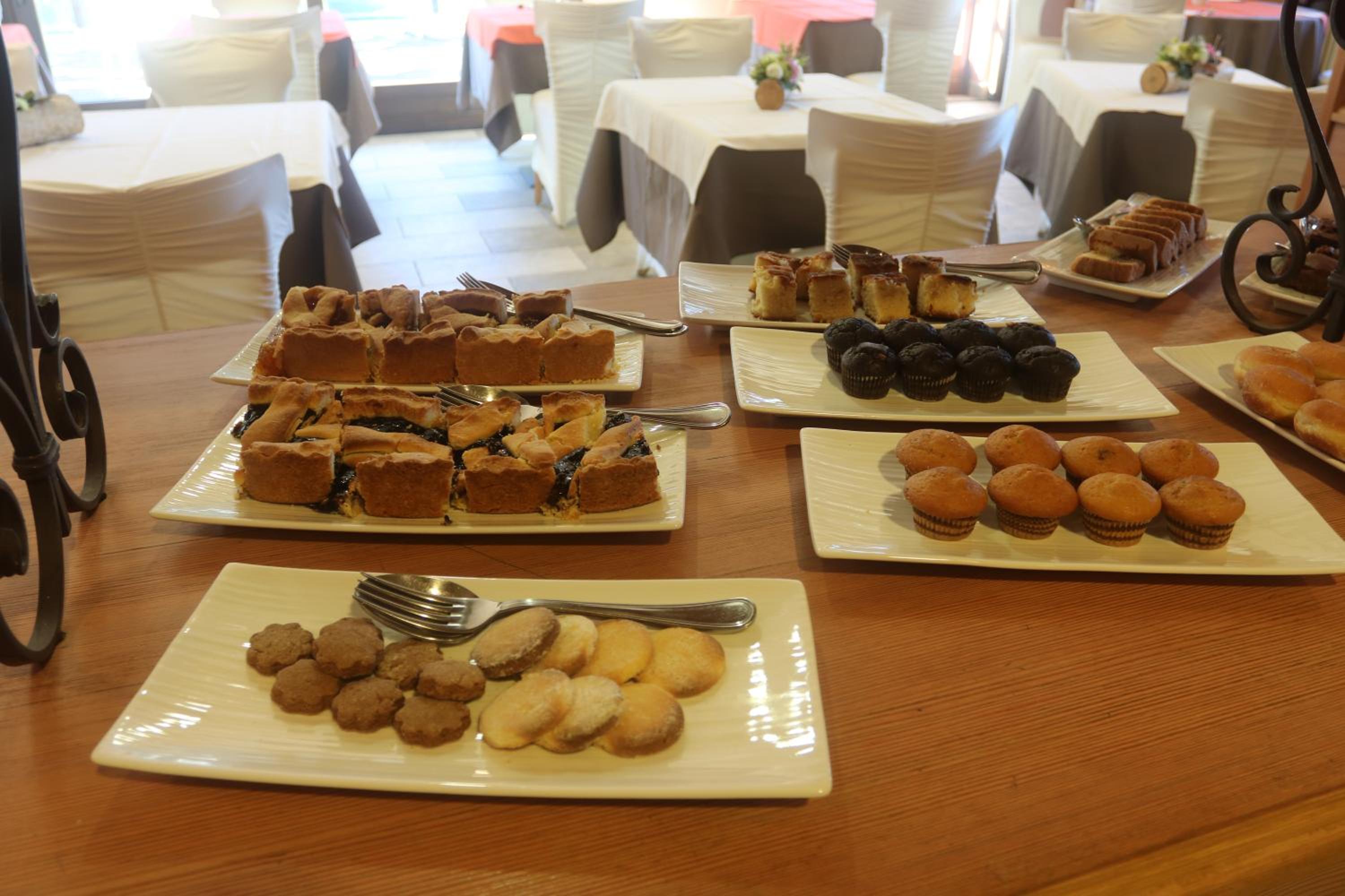 Platters of sliced tarts, muffins, and cookies arranged across a wooden buffet counter in a dining room.