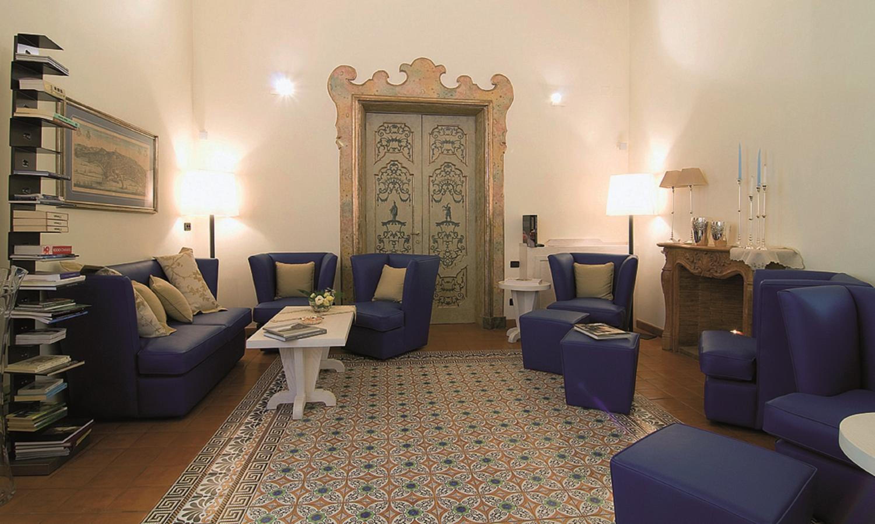 Blue leather armchairs and a matching sofa surround a patterned tile floor in a lounge with a carved doorway.