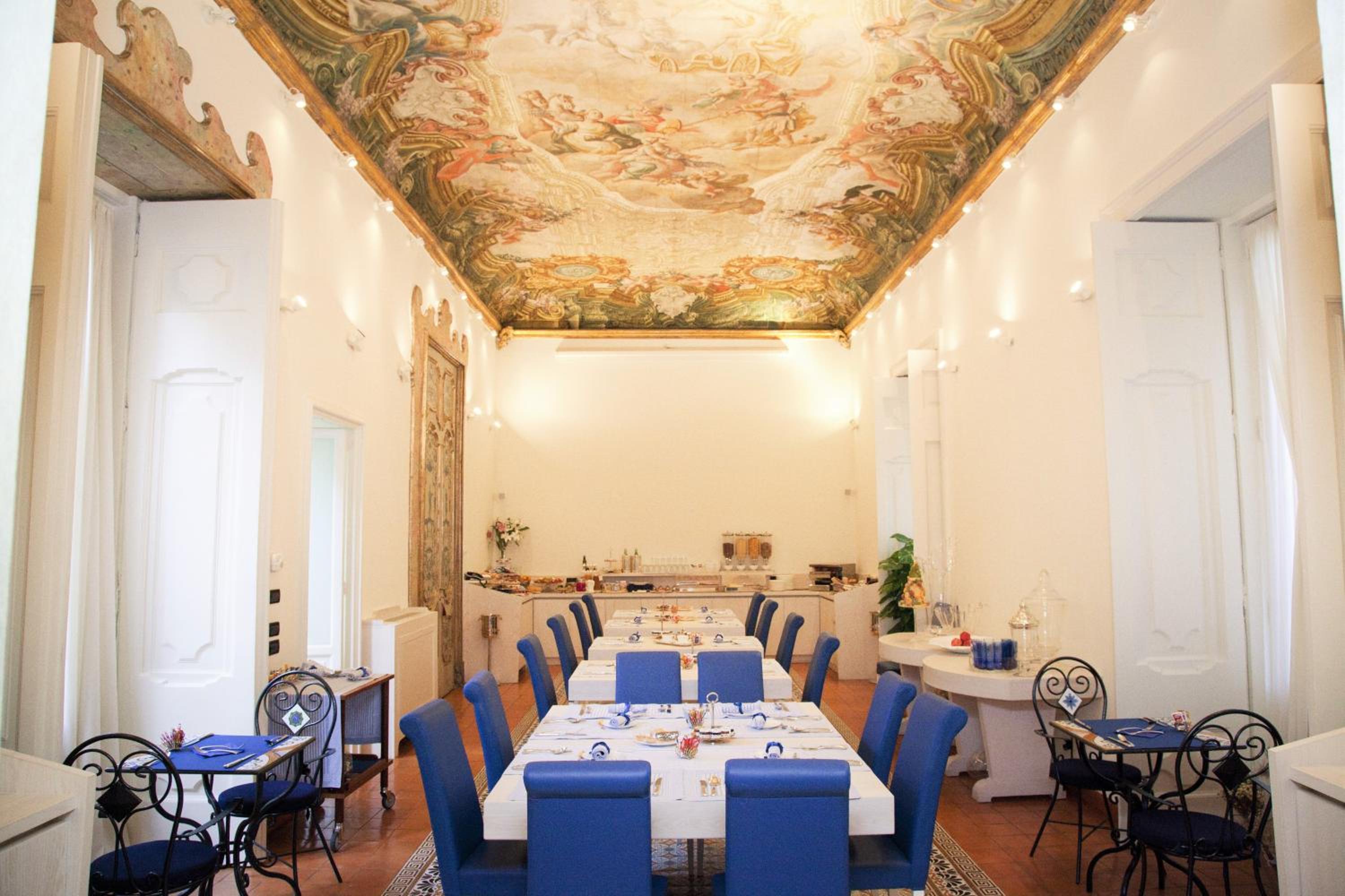 Maison Tofani dining room featuring tables with blue chairs under an ornate frescoed ceiling.