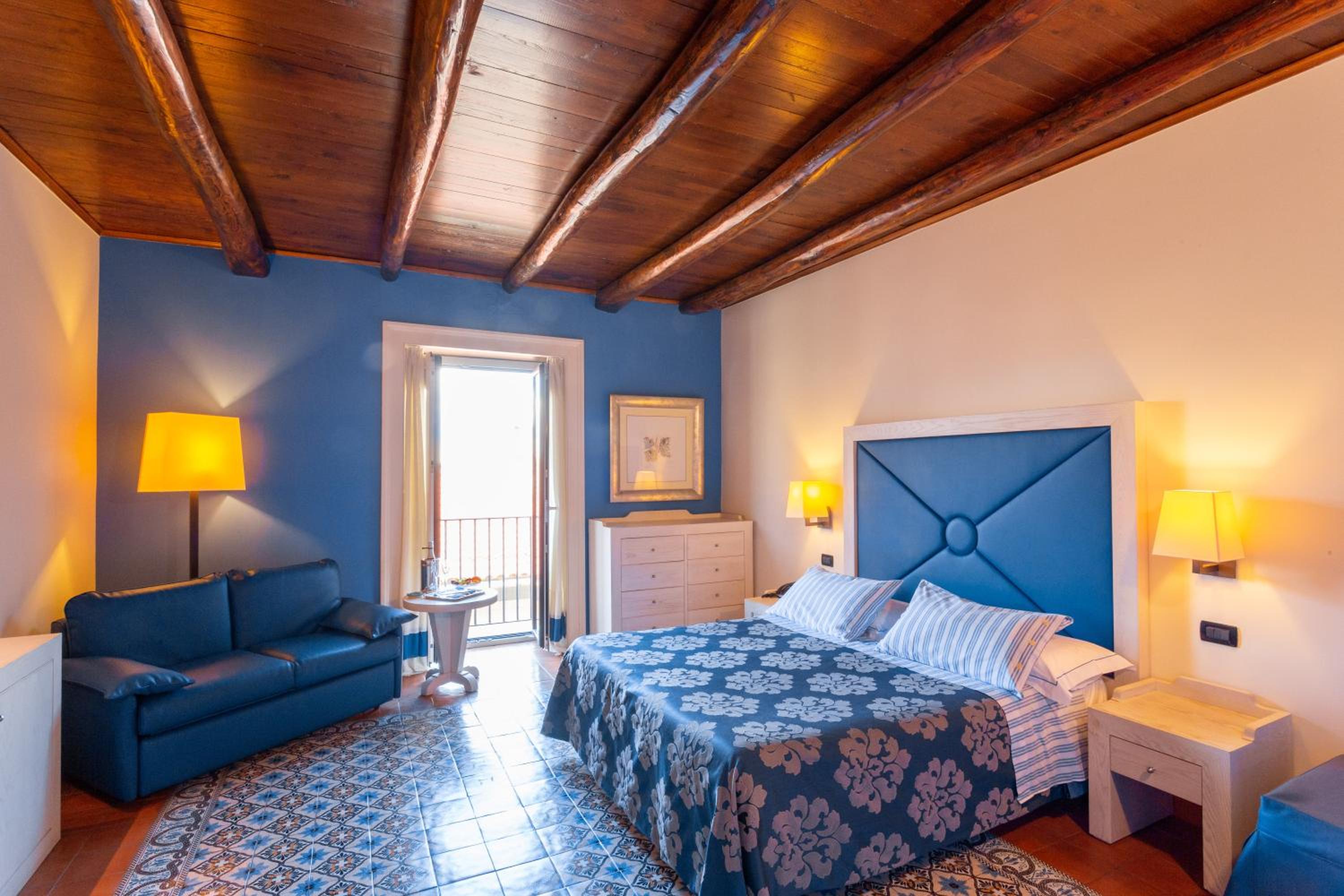 Bedroom featuring a beamed timber ceiling, blue accent wall, patterned tiled floor, and a bed with a blue headboard.