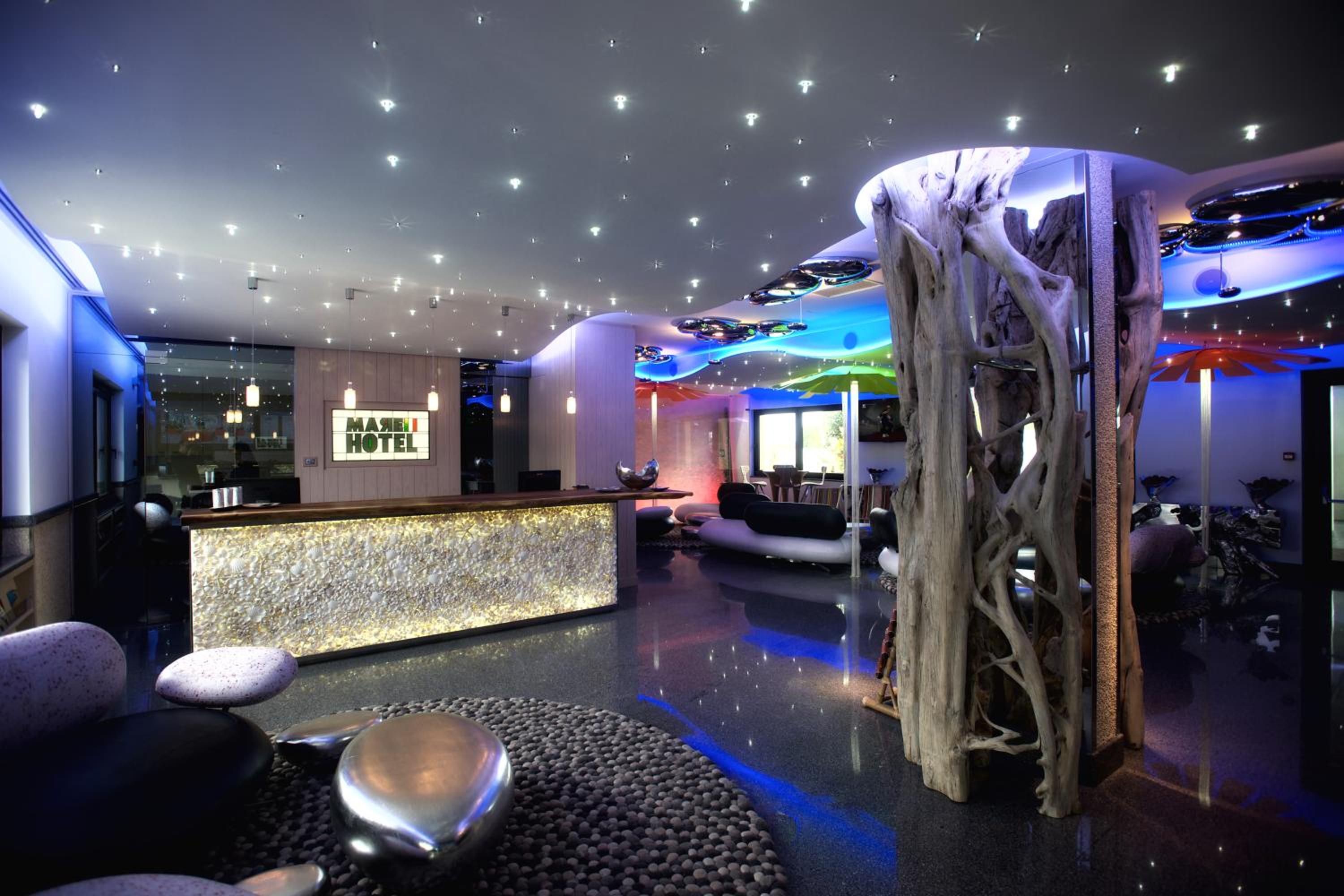 The lobby reception desk glows beneath a star-lit ceiling, beside a sculptural wooden pillar and pebble rug.