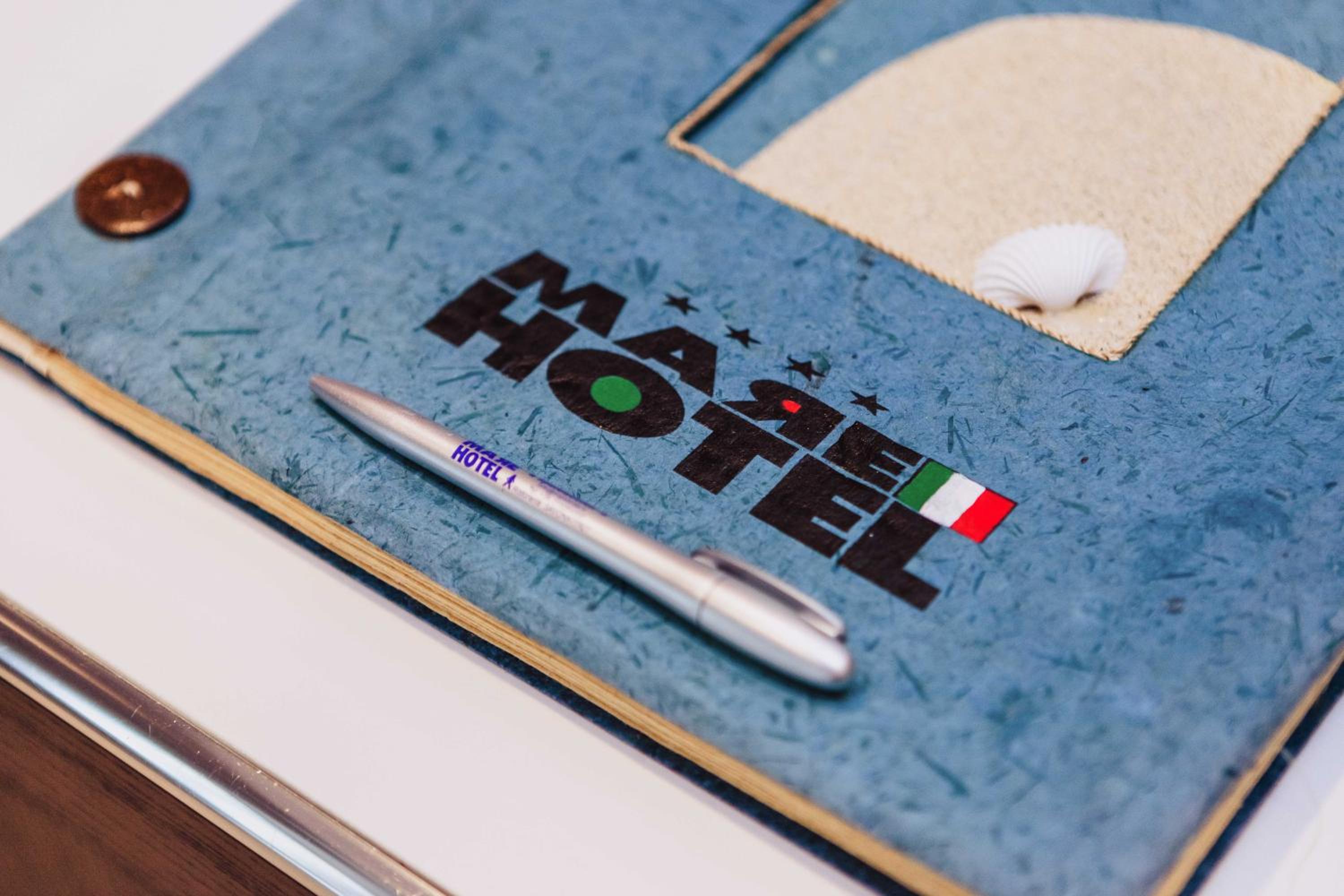 A silver pen rests atop a textured blue guest book featuring a beach motif and logo.