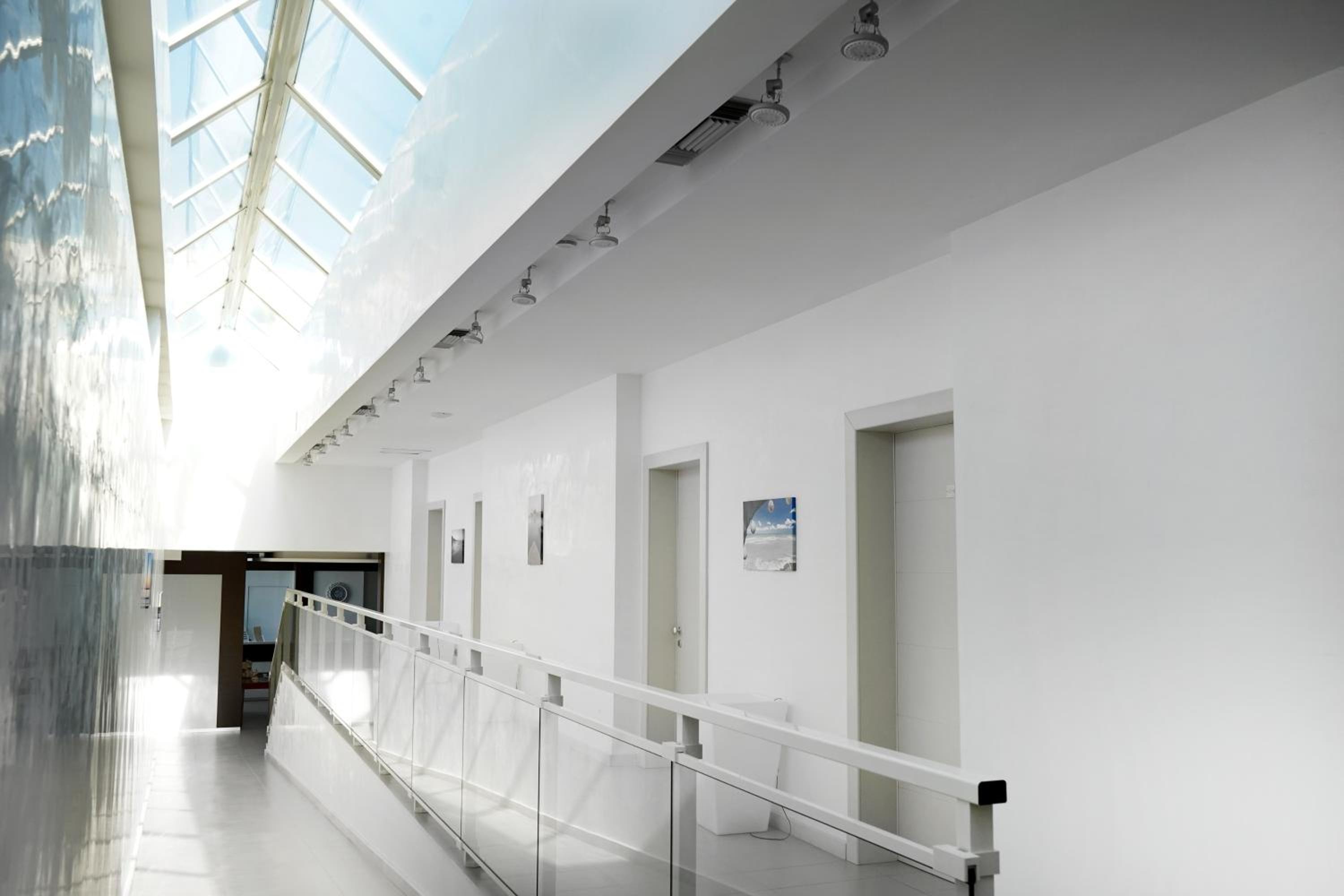 A bright indoor hallway with a glass-paneled ramp, white walls, and an overhead skylight.