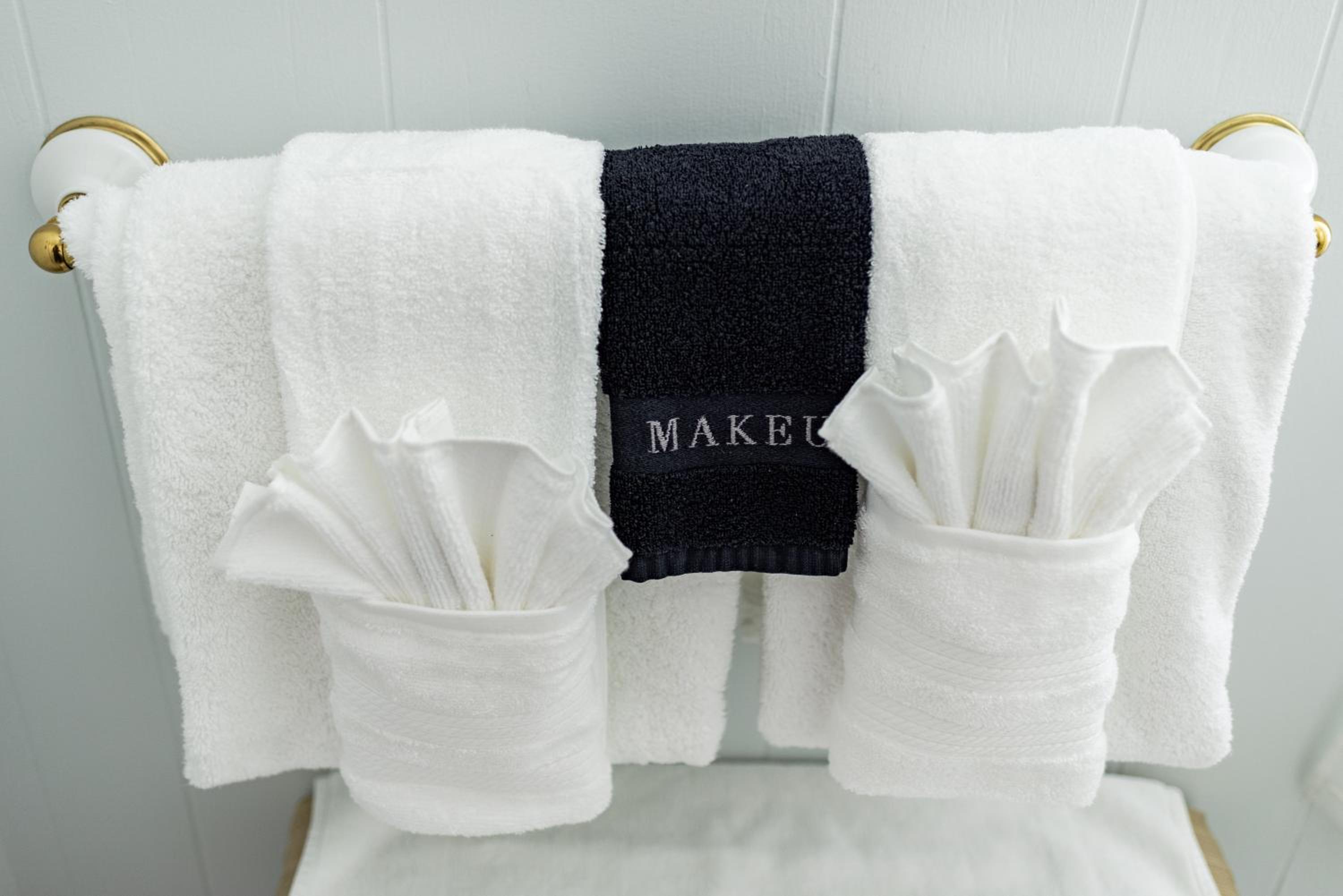 White towels and a dark makeup cloth hang neatly folded on a brass and porcelain wall rack.