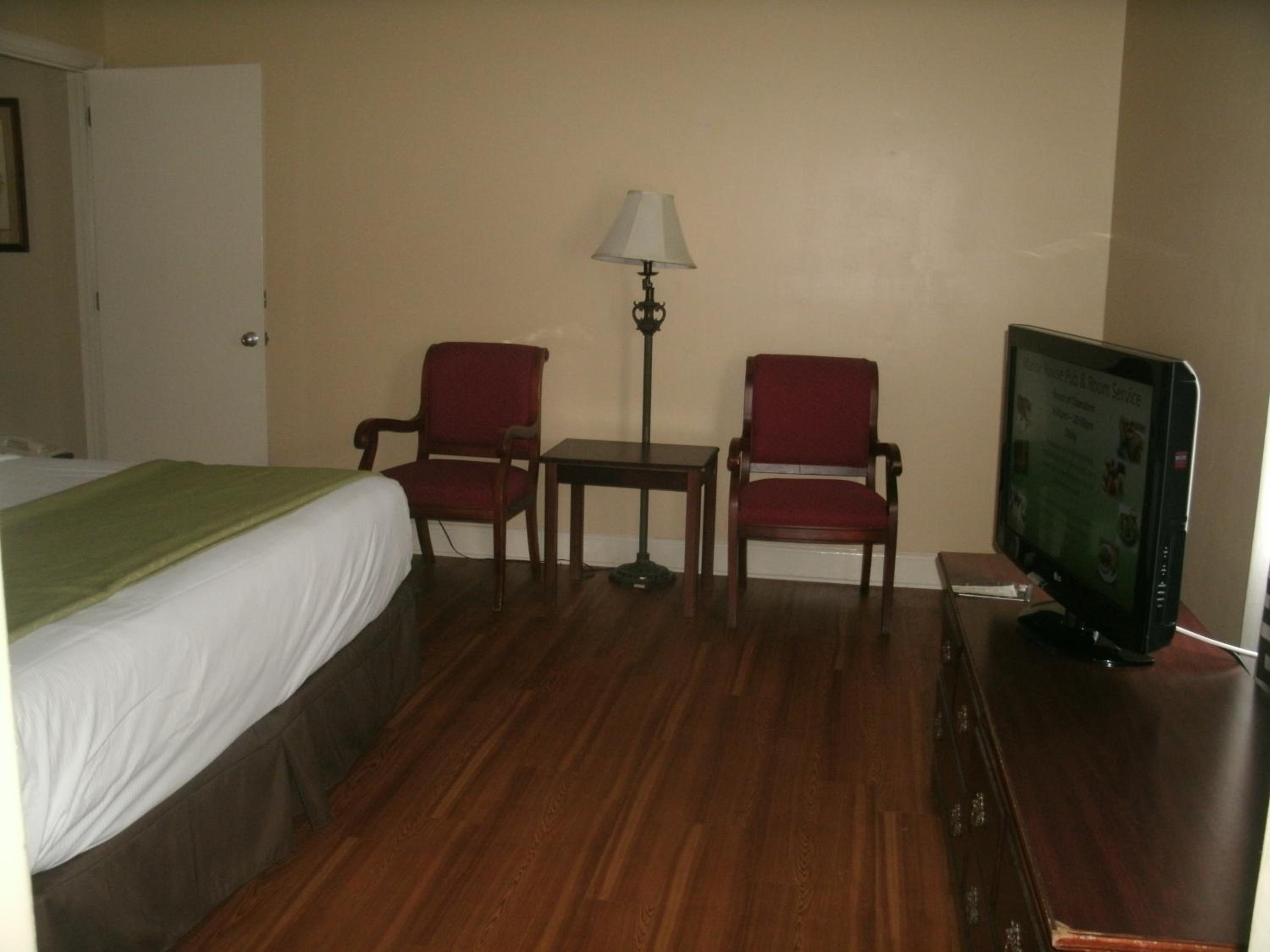 Guest room with wood-laminate flooring, red armchairs flanking a side table with a lamp, and a television on a dresser.