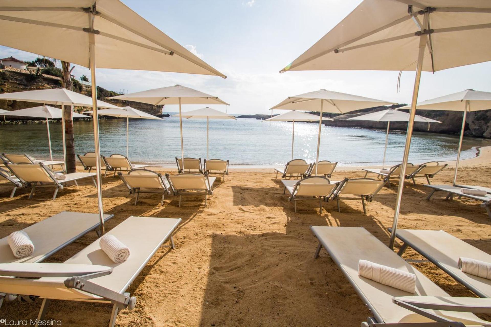 Sun loungers and white parasols set on a sandy beach cove overlooking calm sea.