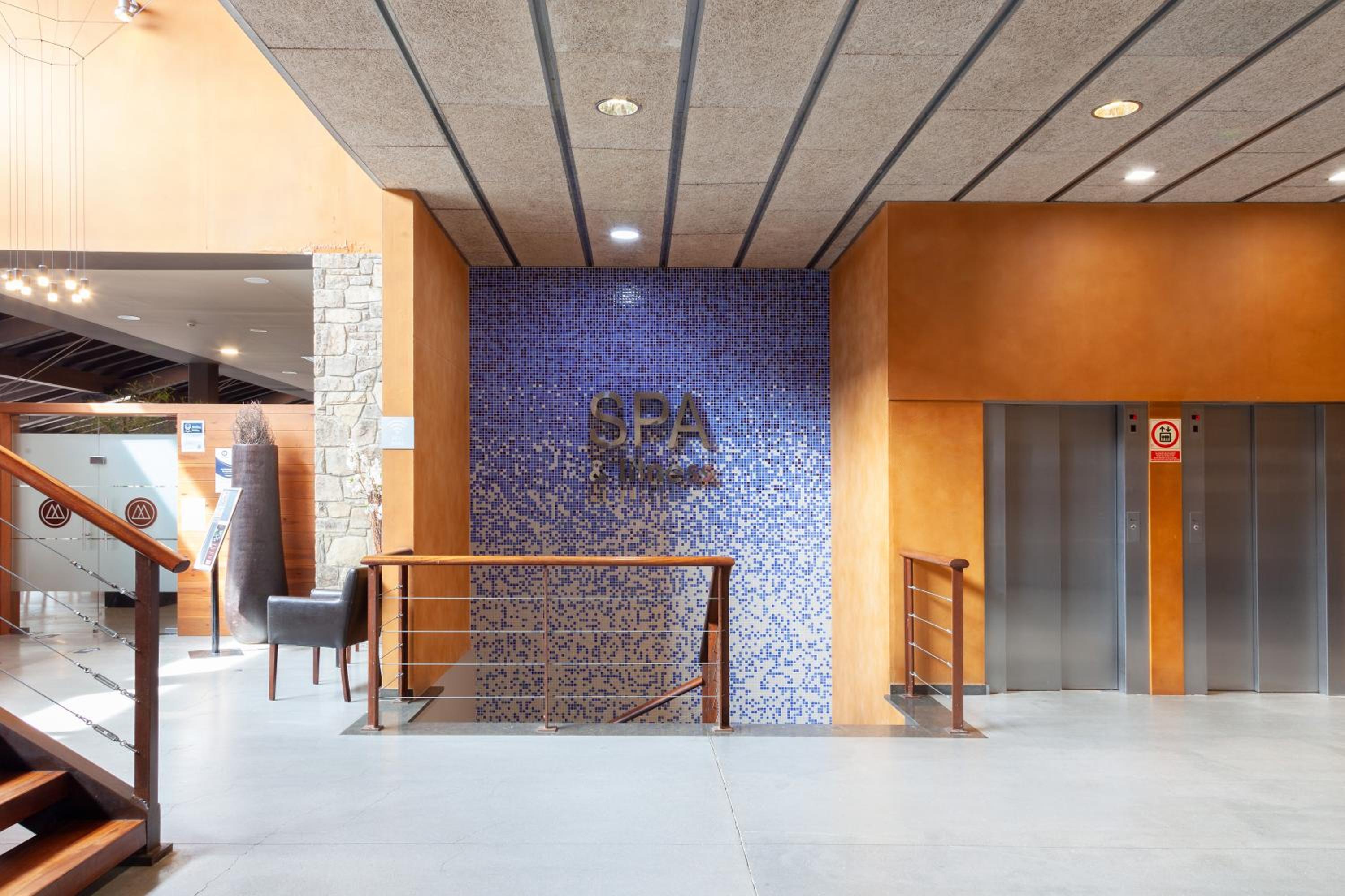 A staircase descending to a spa behind blue mosaic tile, flanked by elevator doors.