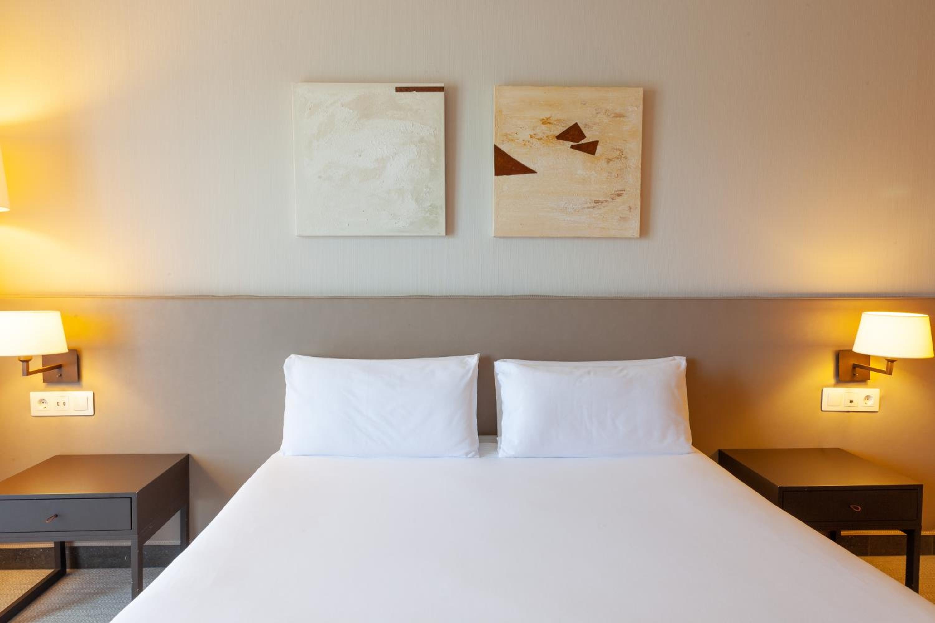 A bedroom with a neatly made bed, neutral headboard, abstract wall artworks, and bedside lamps.