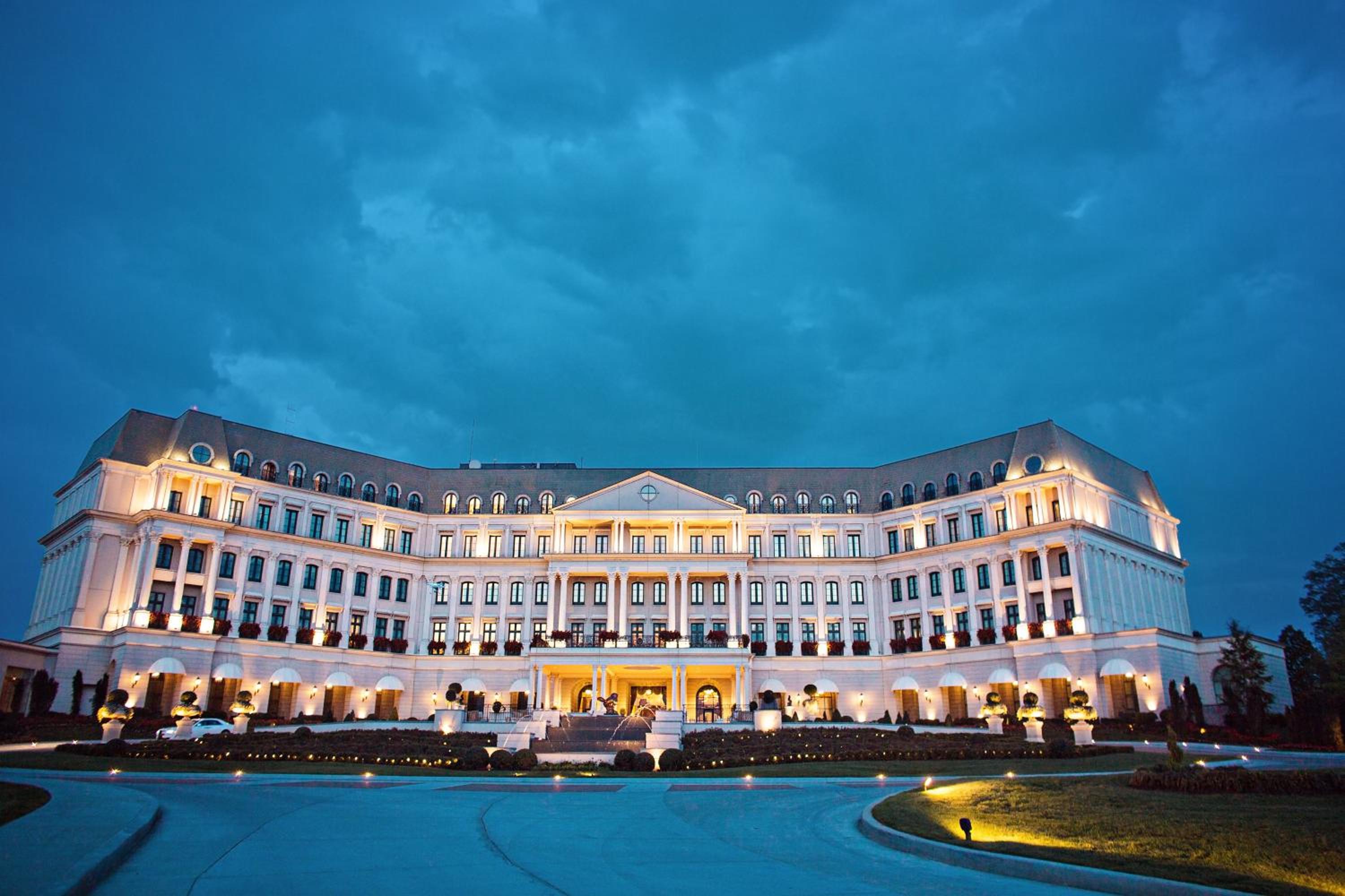Illuminated classical stone facade of Nemacolin with lit windows and a curved driveway at dusk.