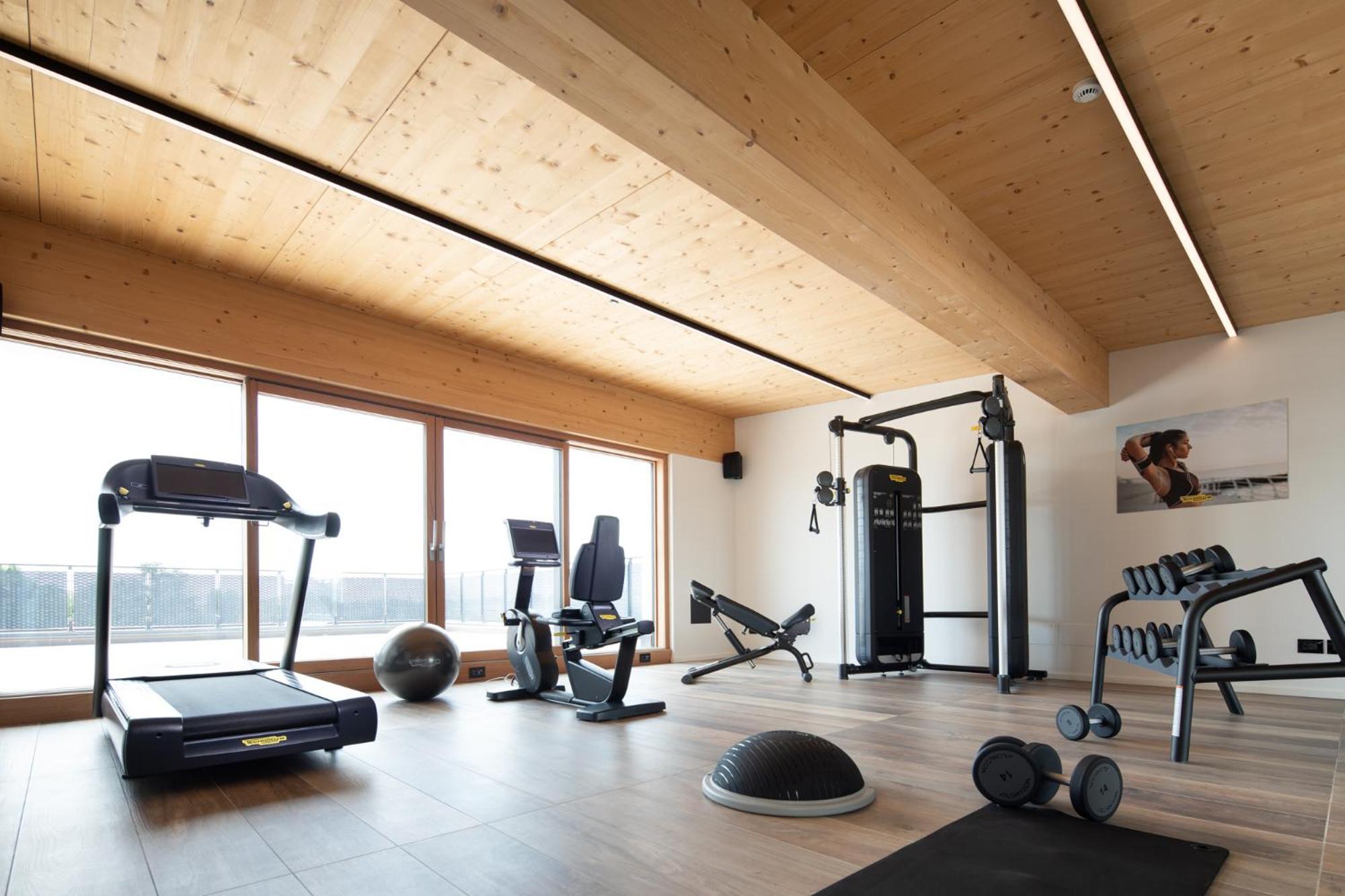 A fitness room with a wood-paneled ceiling, gym equipment, and large glass patio doors.