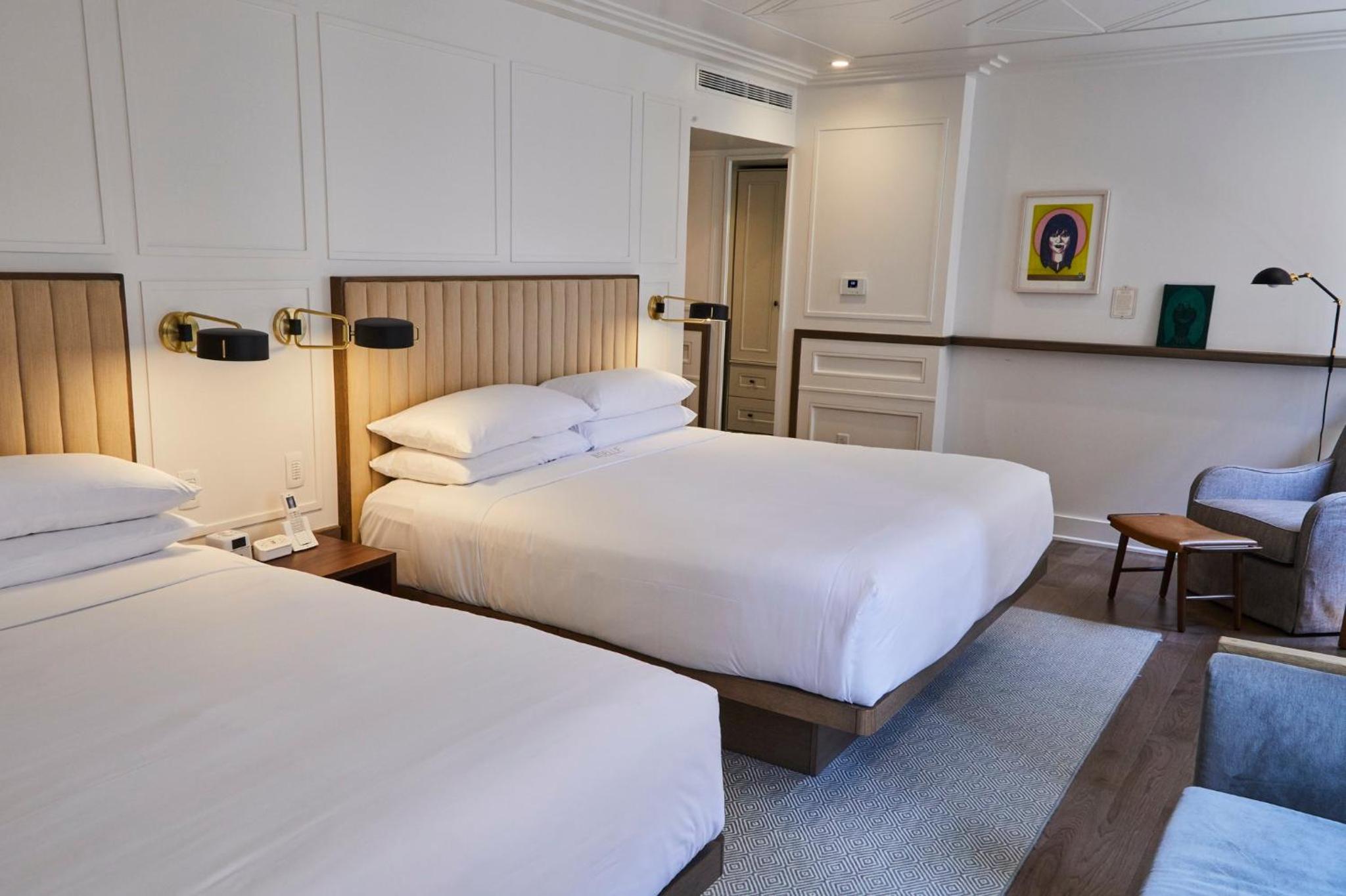 A hotel room at Noelle featuring beds with ribbed headboards, bedside sconces, and white paneled walls.
