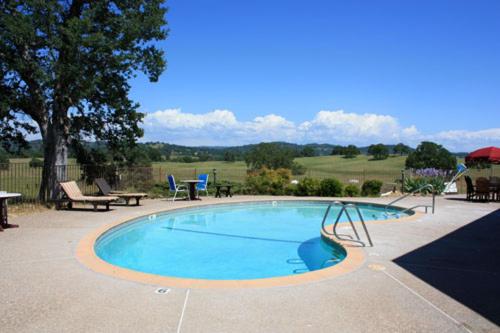 A swimming pool on a concrete terrace overlooking rolling green hills and trees under a bright blue sky.