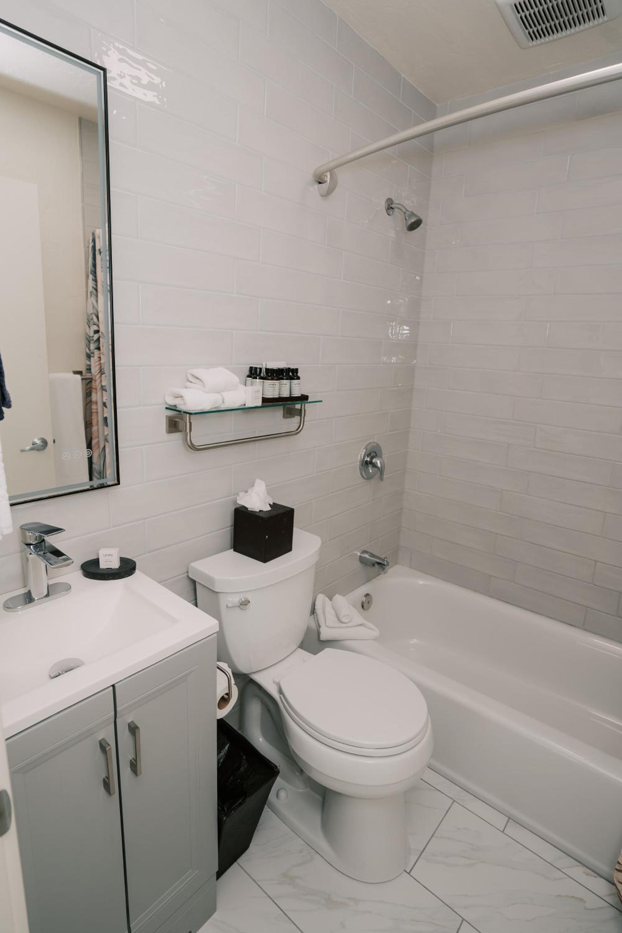 A bathroom features white subway-tiled walls, a porcelain tub, a toilet, and a vanity sink.