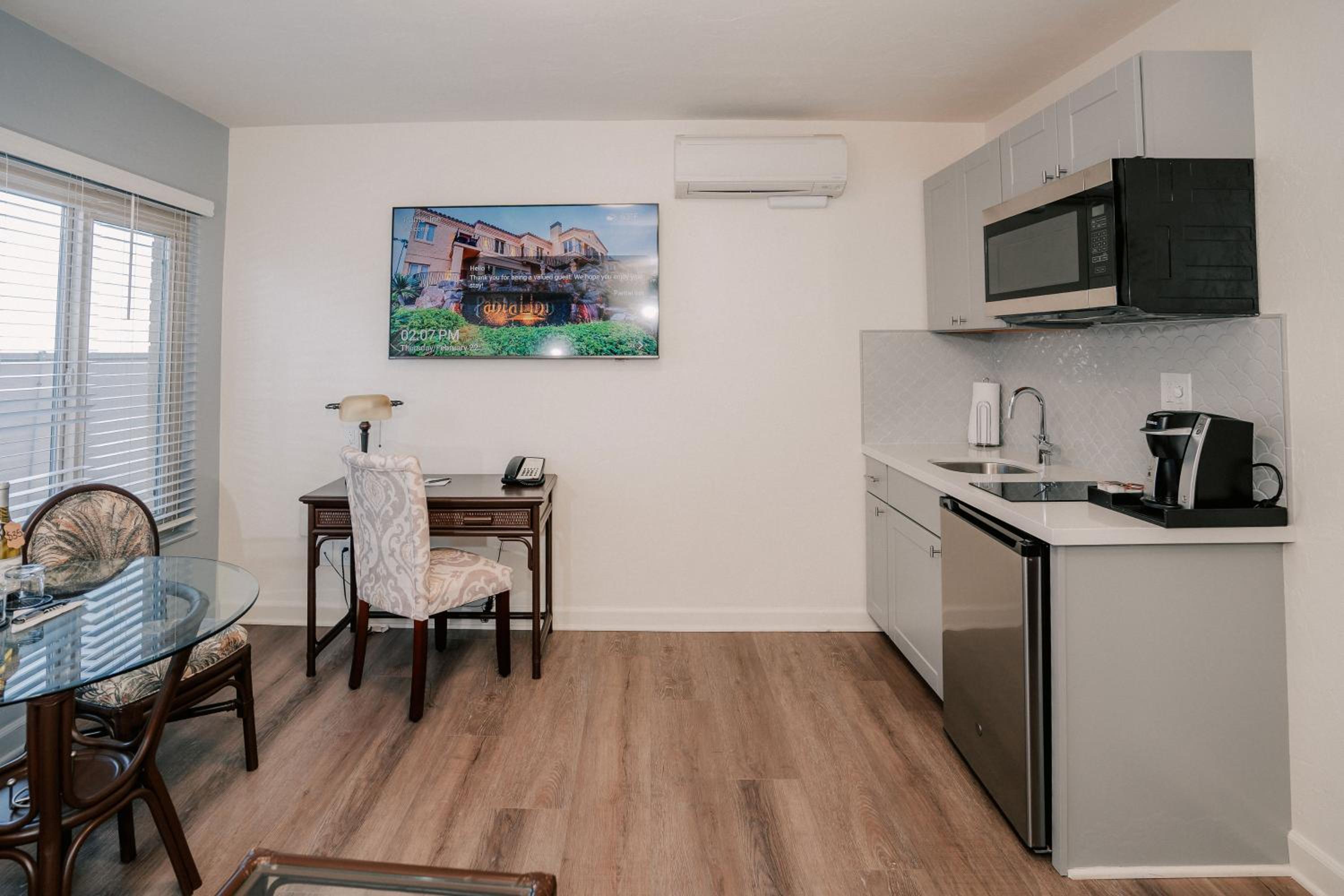 A suite interior features a kitchenette counter, a small wooden work desk, and wood-look flooring.