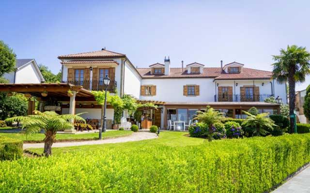 Facade of Pazo do Rio with white walls, terracotta tile roof, lawn, and trimmed hedges under a clear sky.