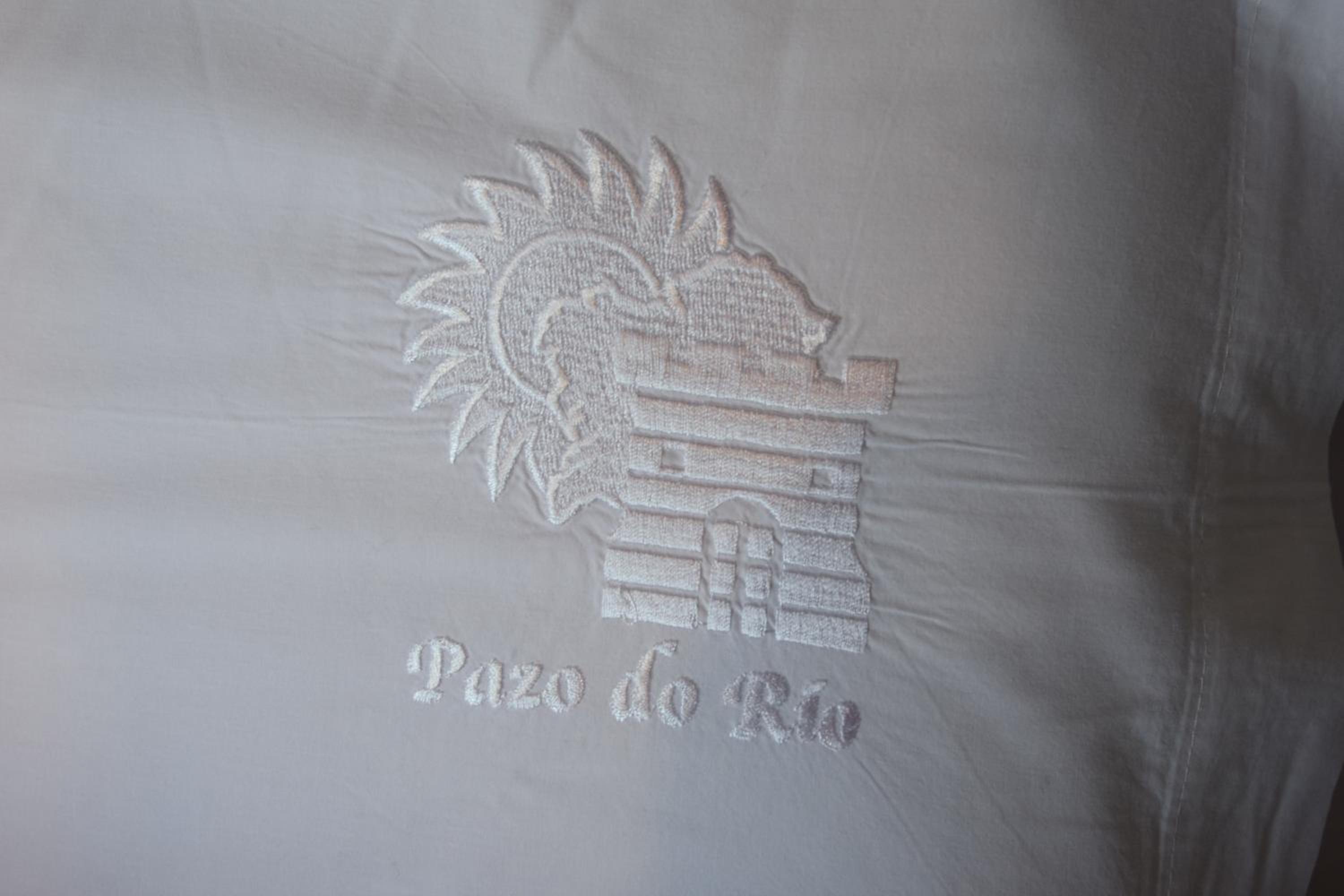 White fabric embroidered with a fortress crest and Galician lettering.