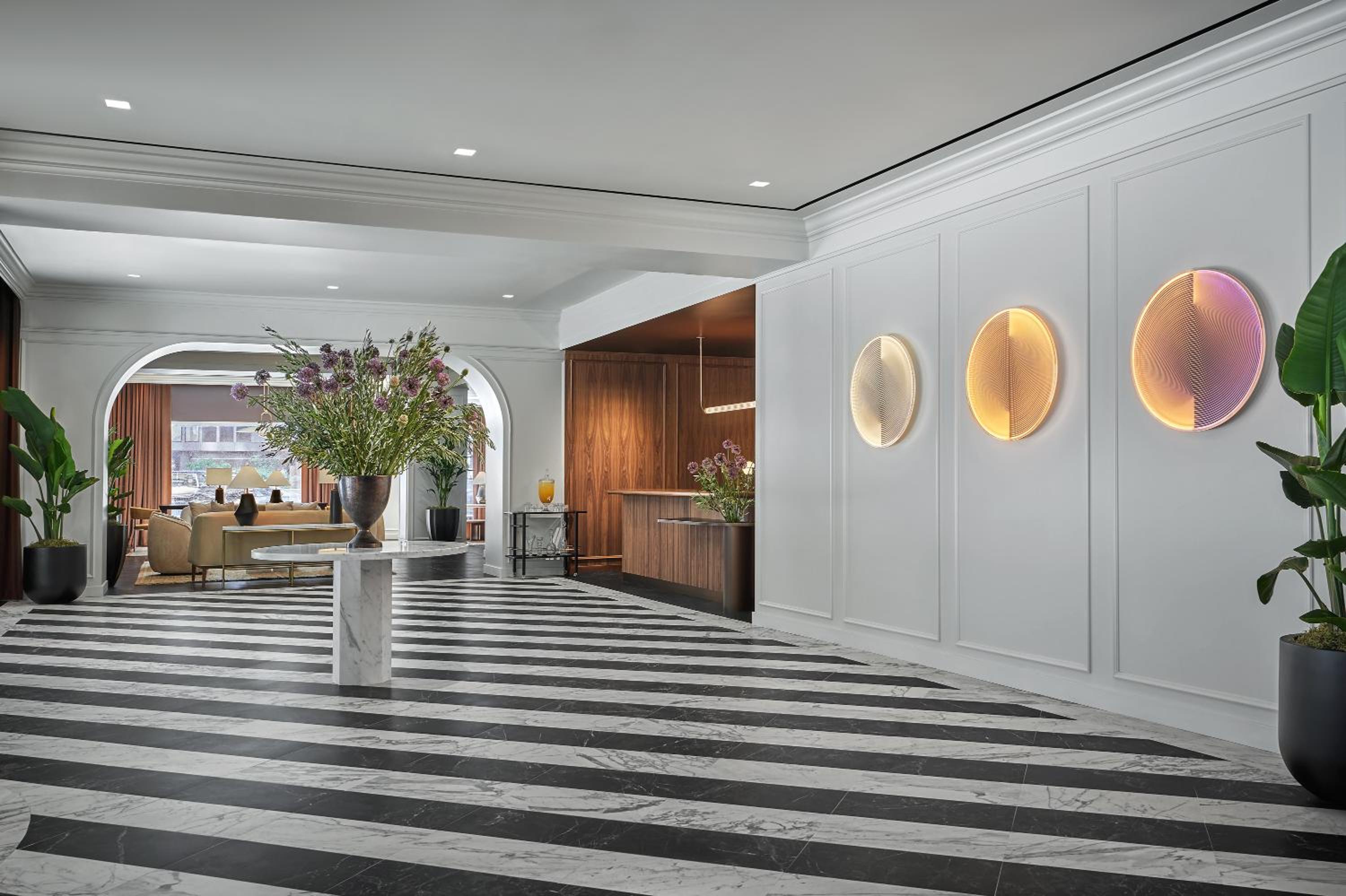 Lobby with diagonal striped marble floors, a tall floral arrangement, and illuminated circular wall sculptures.