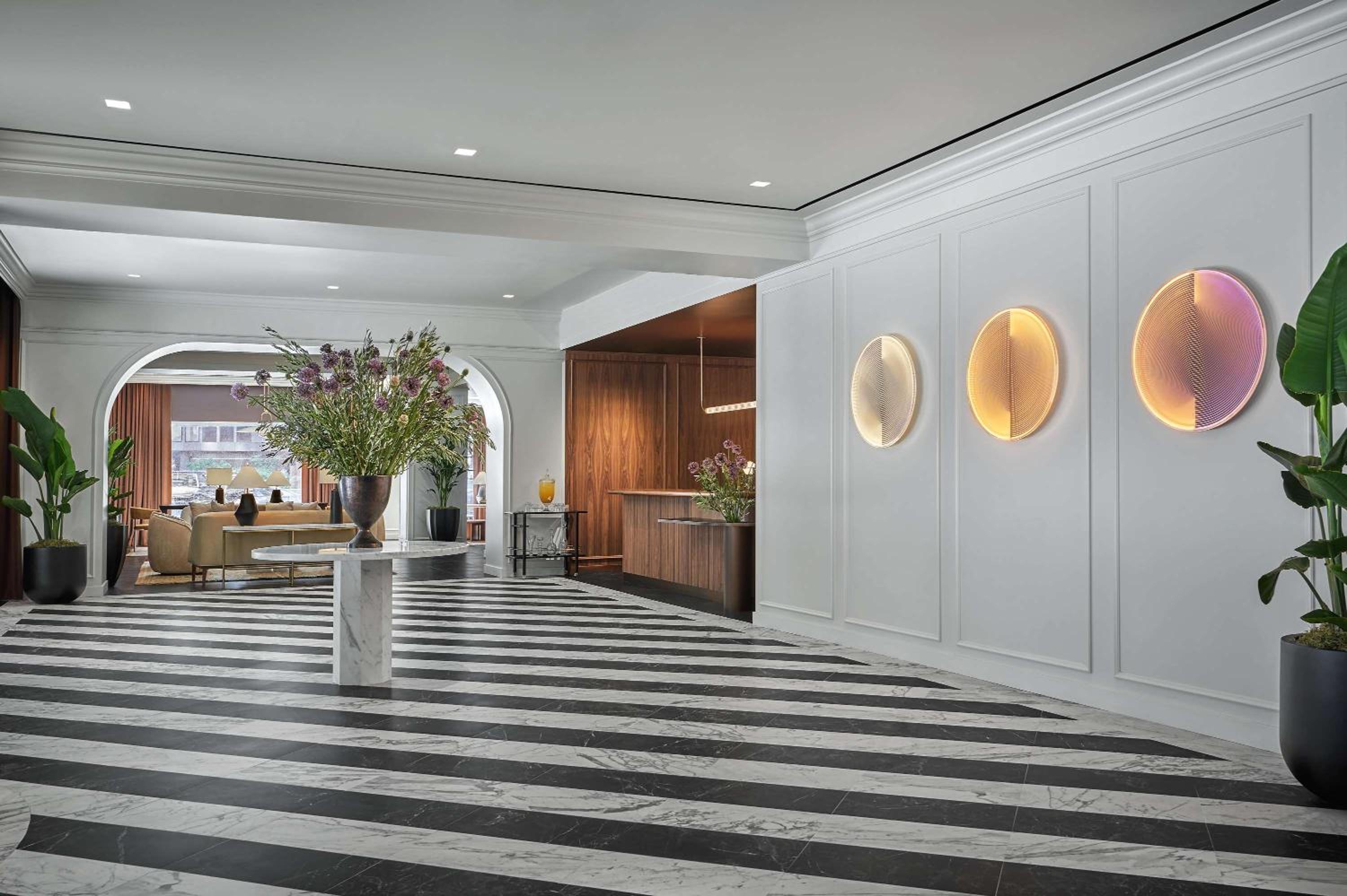 Hotel foyer showing striped marble floor tiles, a reception desk, and glowing disc artwork along white walls.