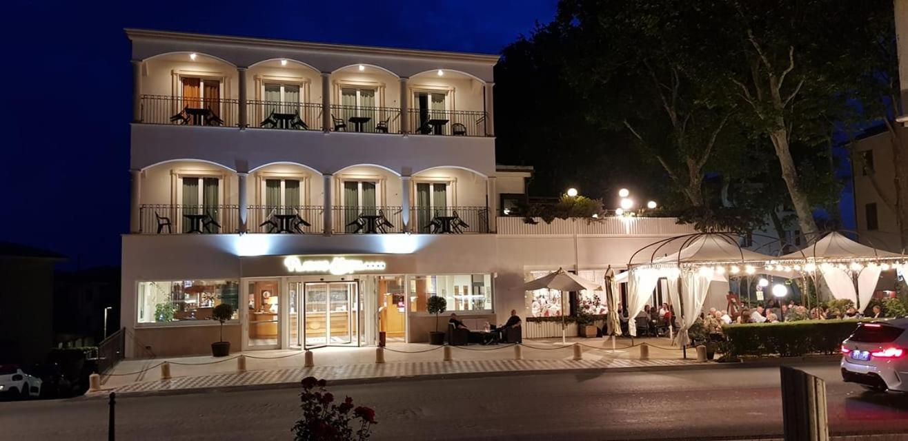 Illuminated facade of Platani Hotel at night with arched balconies and an outdoor covered dining terrace.