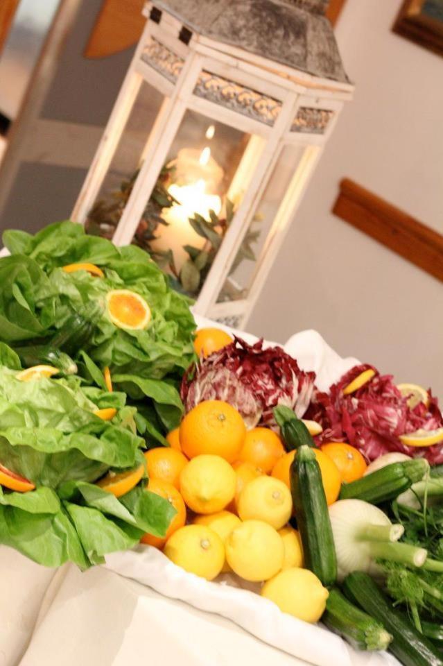 Fresh lettuce, citrus fruits, radicchio, and zucchini arranged in a bowl beside a white decorative candle lantern.
