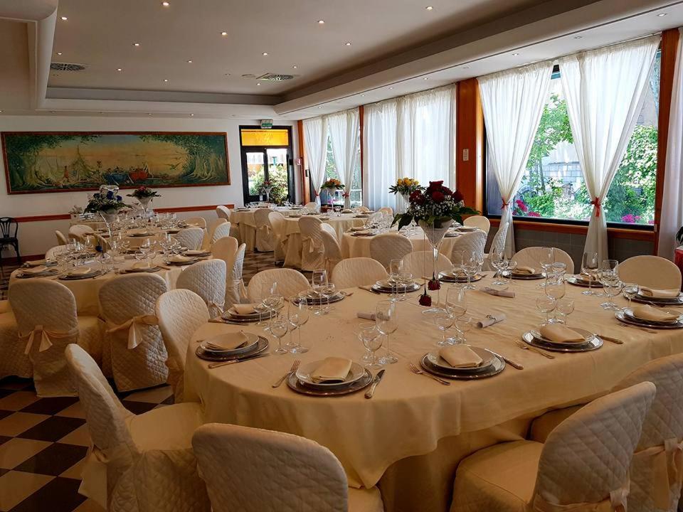 Banquet hall arranged with cloth-covered round tables, floral centerpieces, and sheer white curtains.