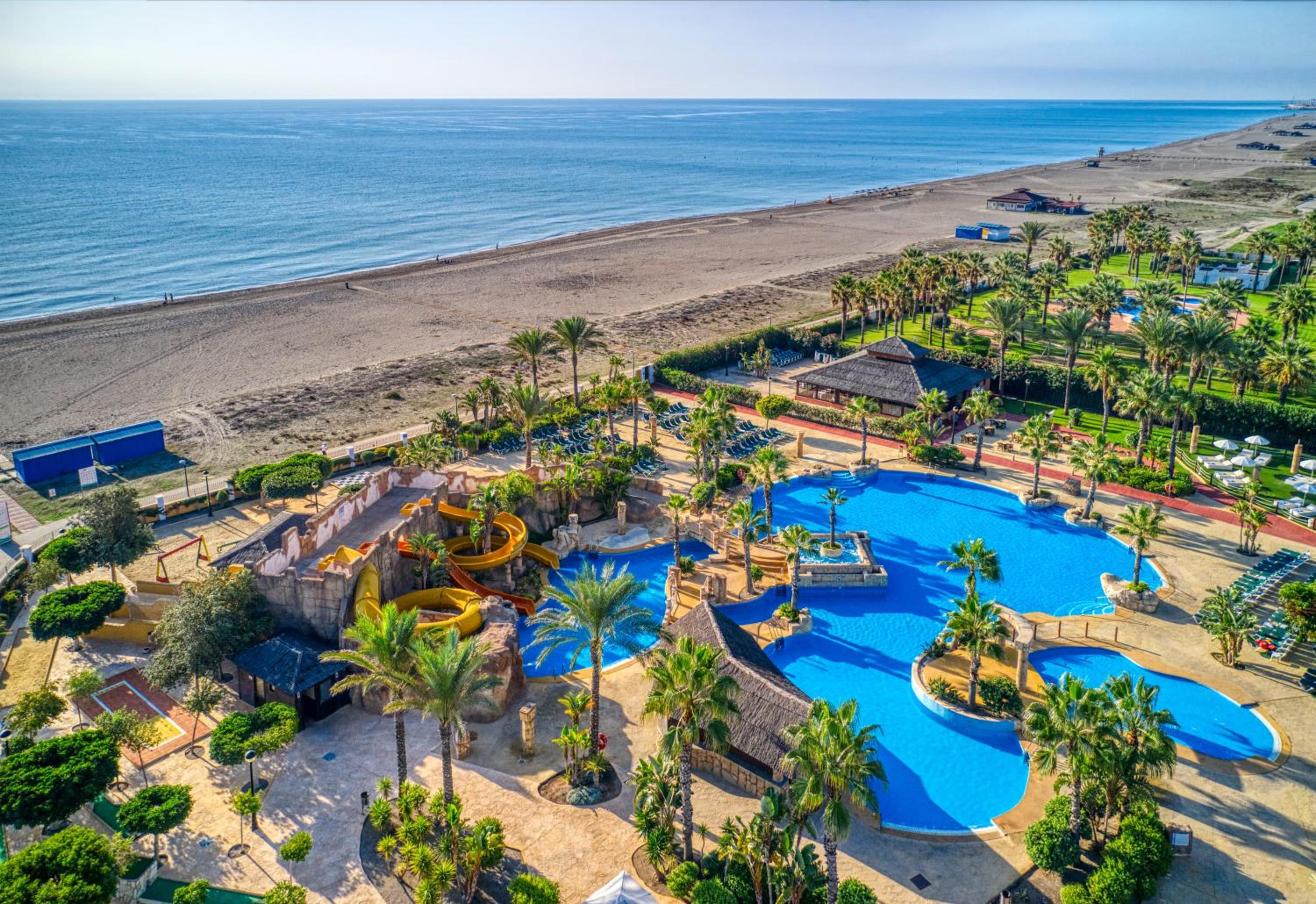 Aerial view of Playazimbali resort pools, water slides, palm trees, and a sandy beach leading to the sea.