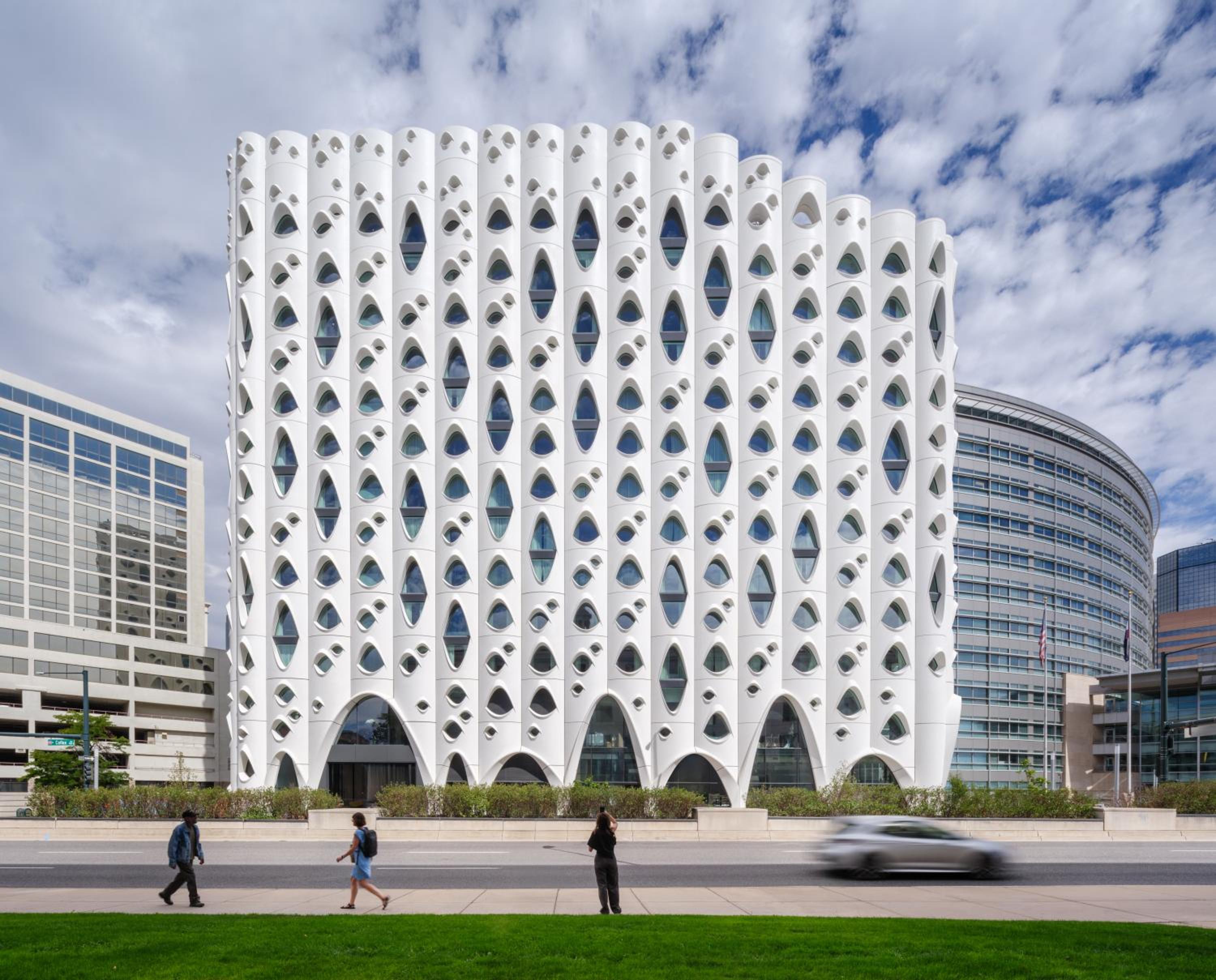 Exterior view of Populus Denver featuring a sculptural white facade with eye-shaped windows beside a city street.