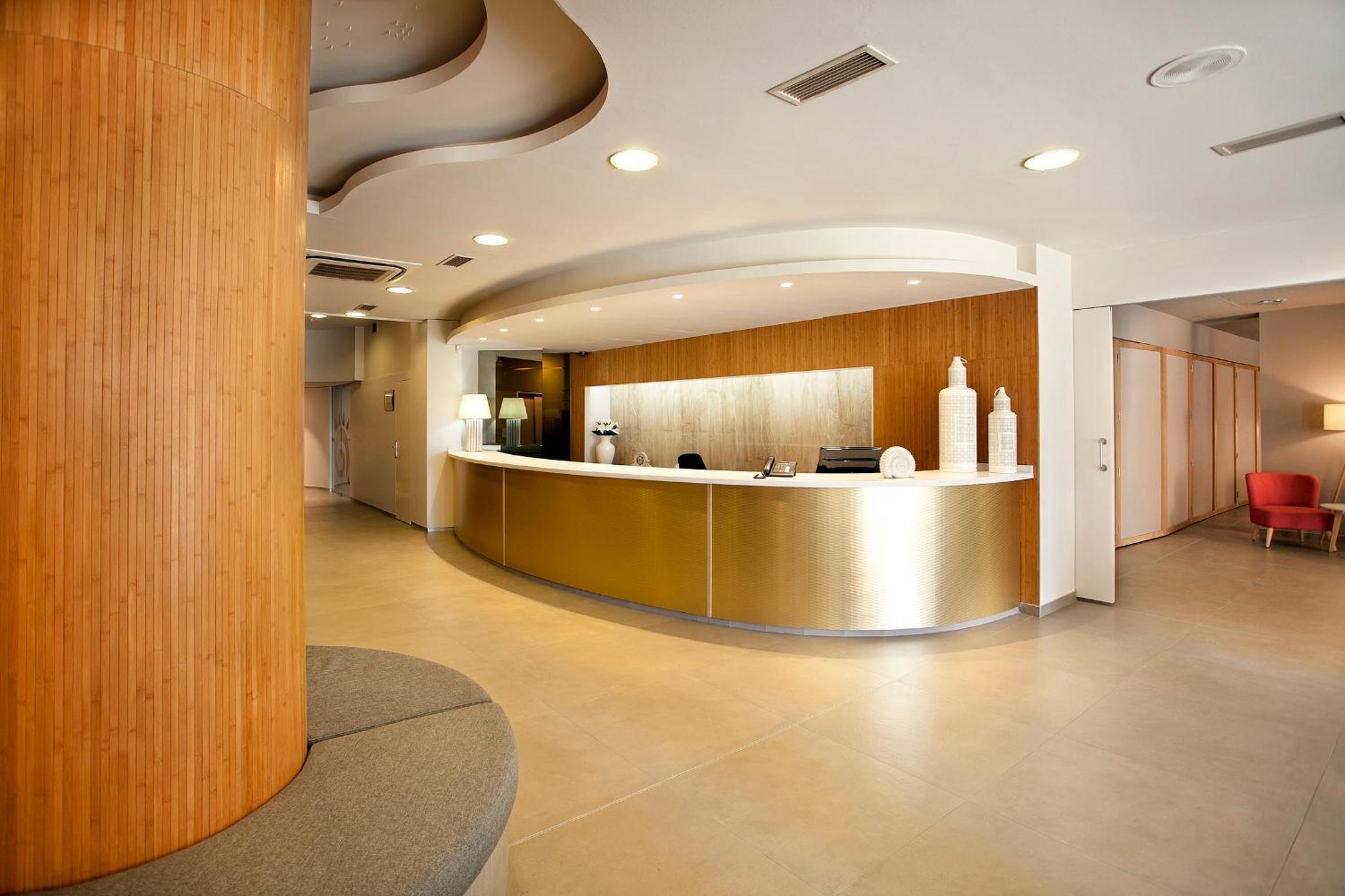 A reception lobby with a curved gold front desk, wood wall paneling, and a circular padded bench.