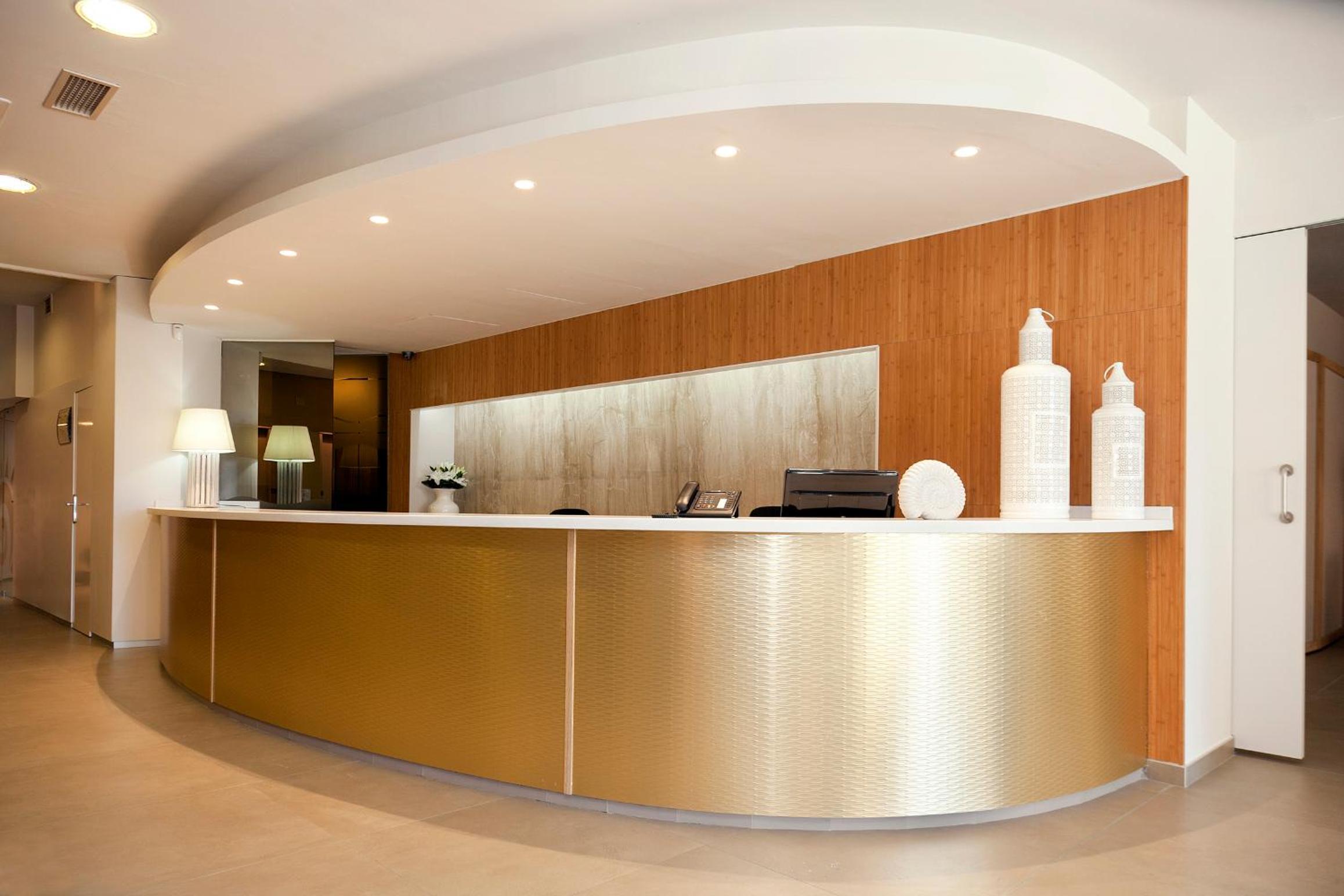 A curved metallic reception desk with a wood-paneled accent wall, recessed downlights, and ceramic vases.