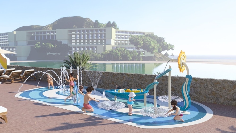An outdoor splash pad with fountains, interactive water elements, and children playing by the sea.