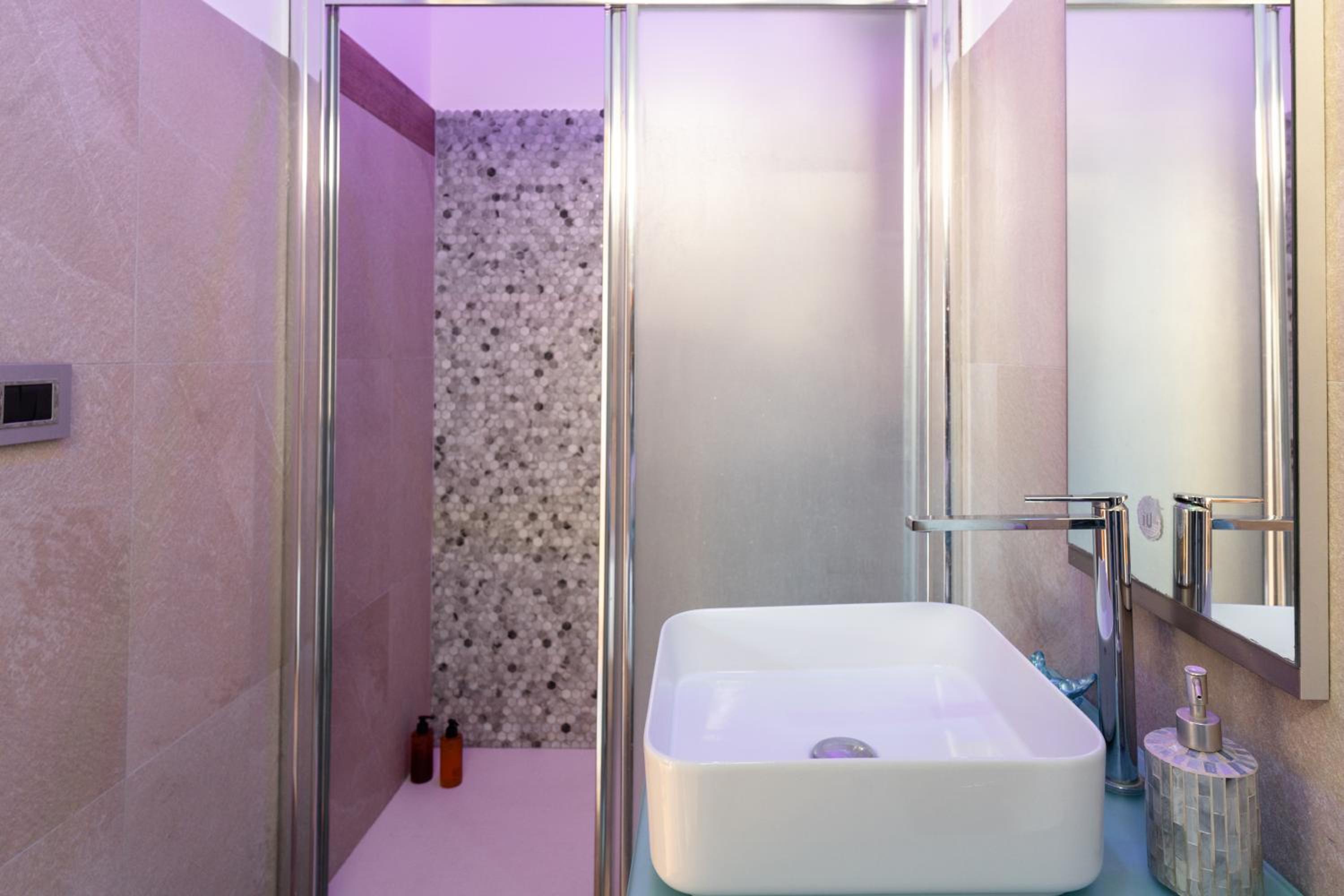Modern bathroom featuring a white vessel sink, chrome faucet, and glass shower enclosure with mosaic tile.