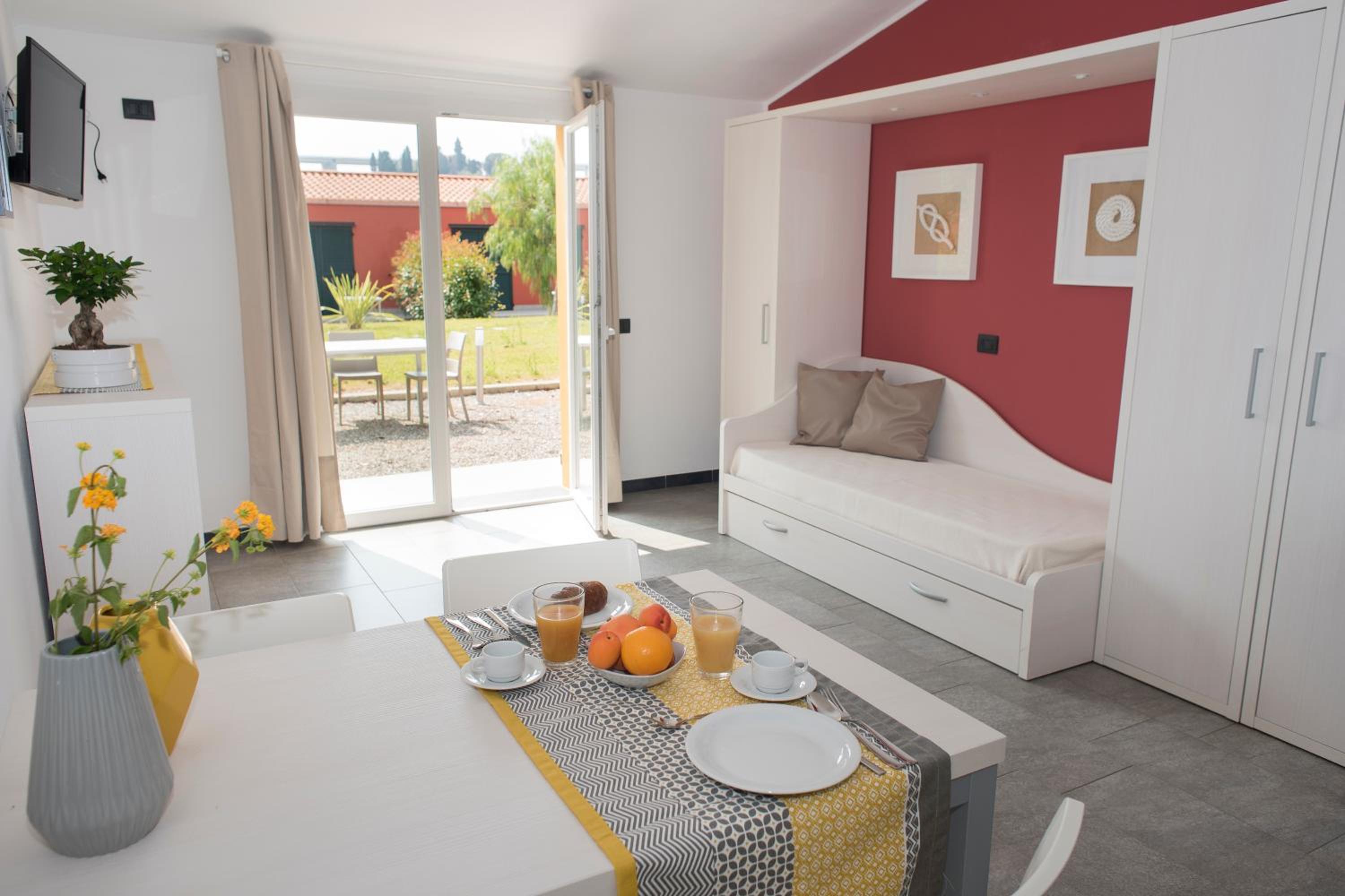 A dining table set for breakfast inside a studio apartment, opening onto a garden patio.