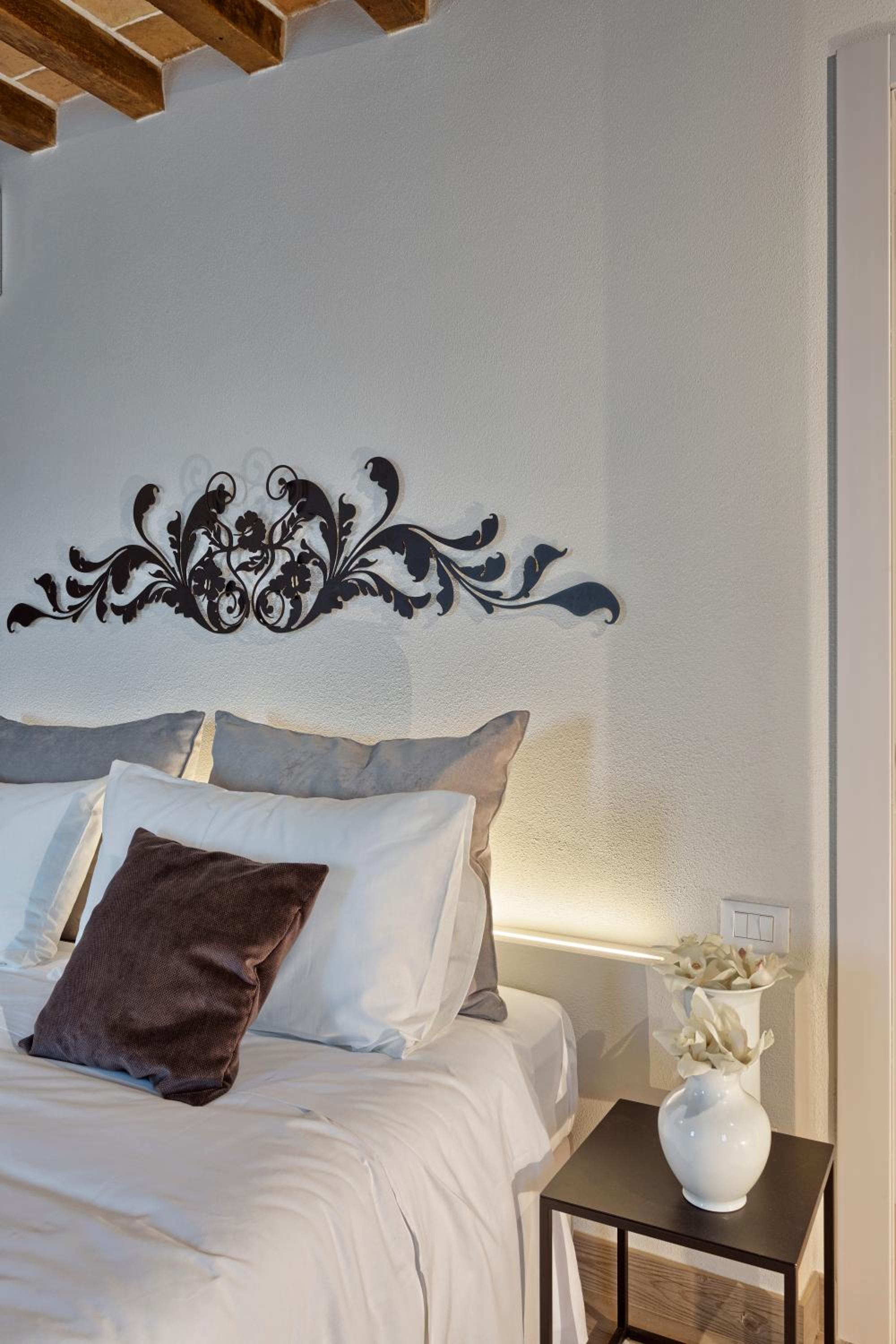 A bed with neutral pillows sits beneath black scrolled metal wall decor and a beamed ceiling.