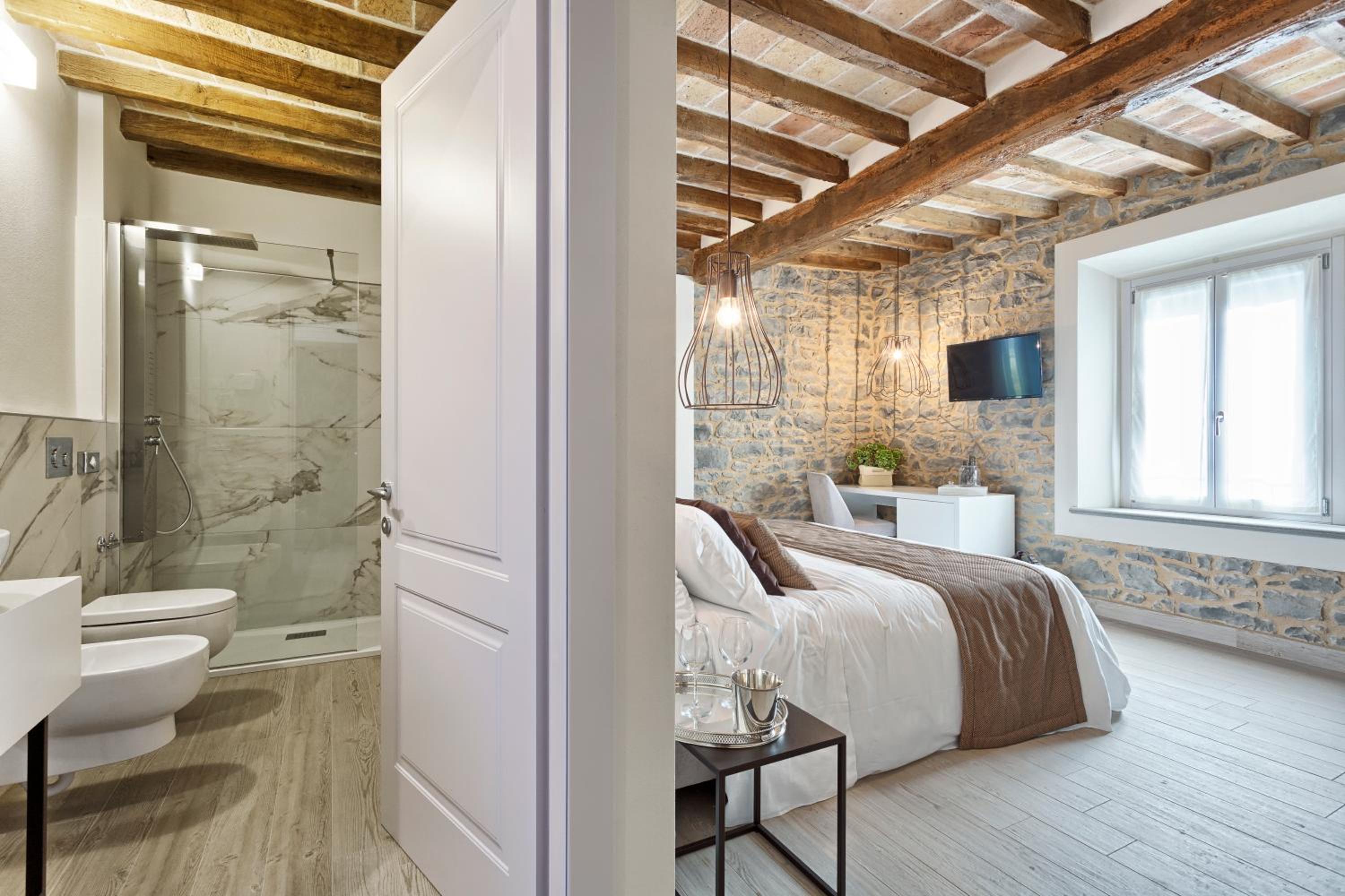 An open doorway frames an ensuite bedroom with stone masonry walls, timber beams, and a modern bathroom.