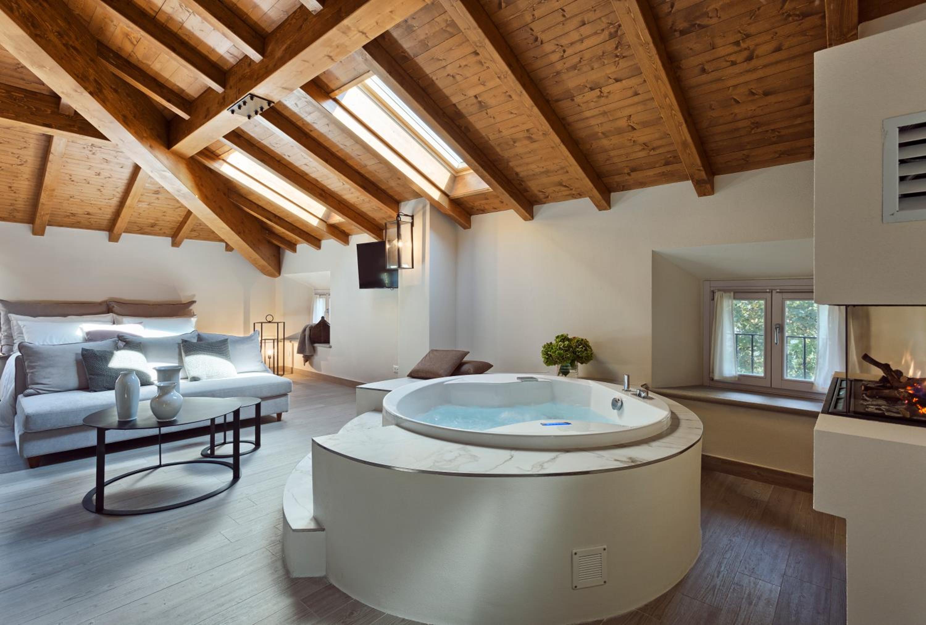 A circular whirlpool tub sits beneath an exposed wood ceiling with skylights in an open bedroom suite.
