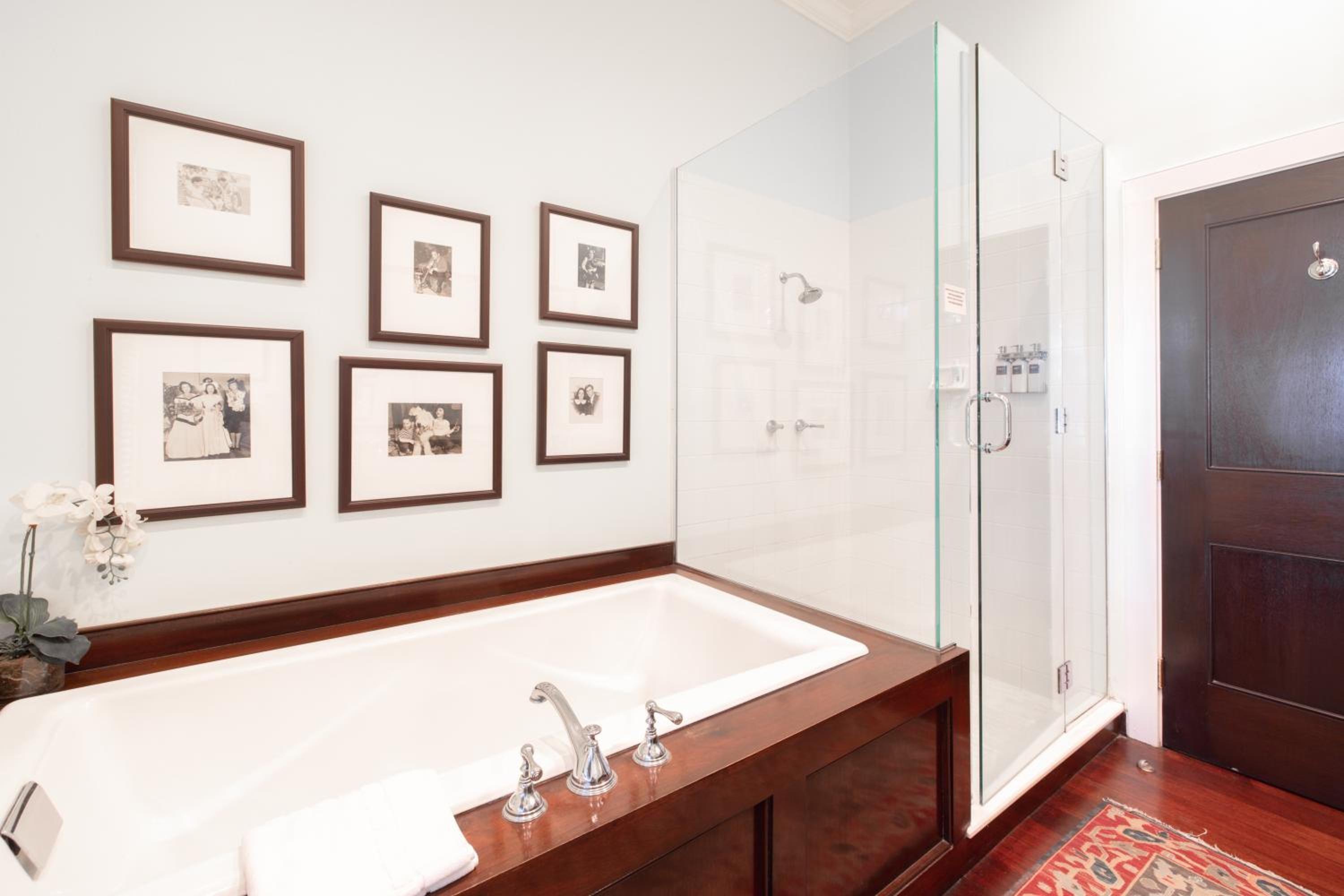A bathroom with a wood-paneled soaking tub, framed monochrome prints on the wall, and a glass shower.
