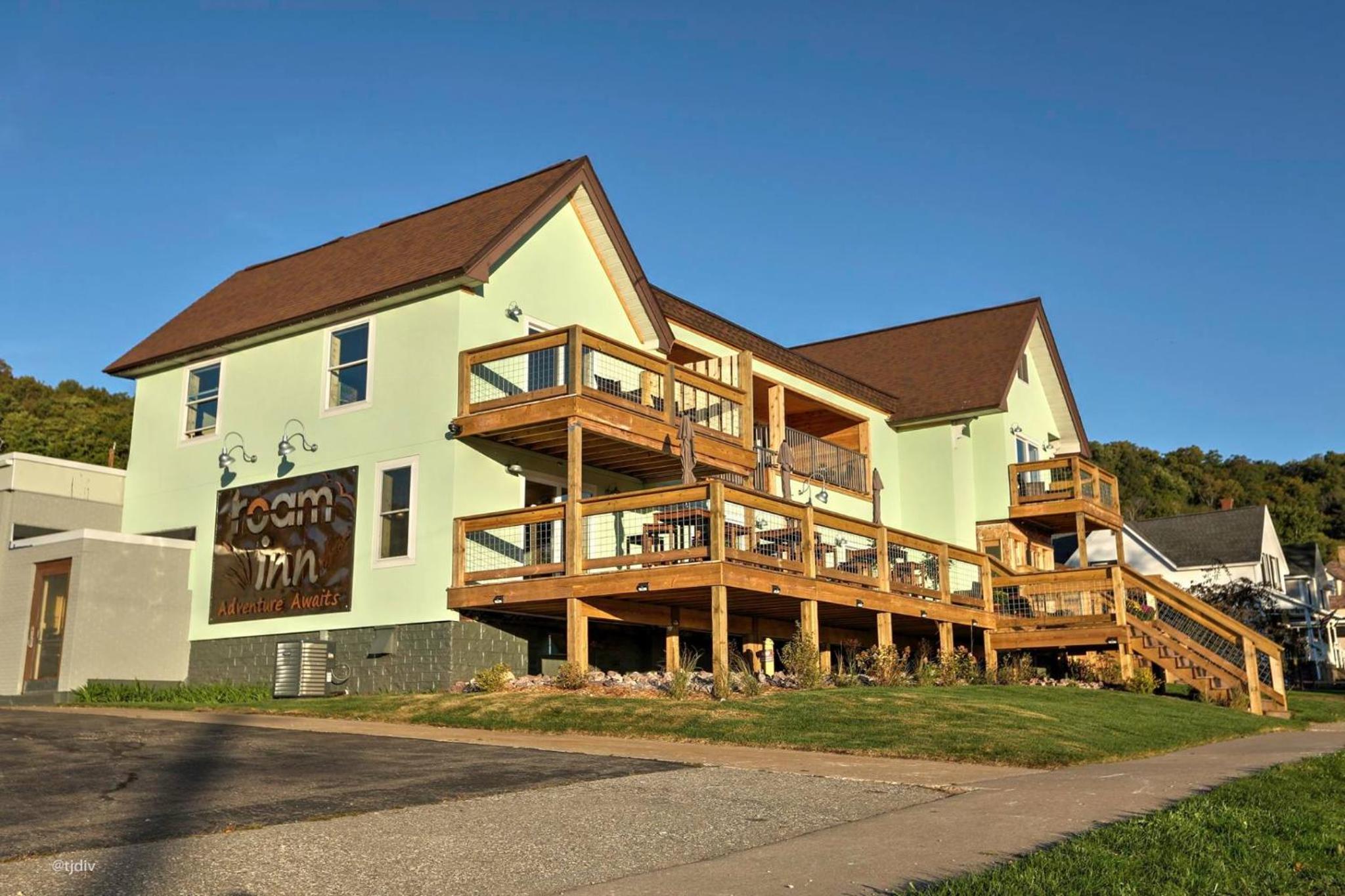 Pale green facade and multi-tier wooden decks of the Roam Inn under a clear blue sky.