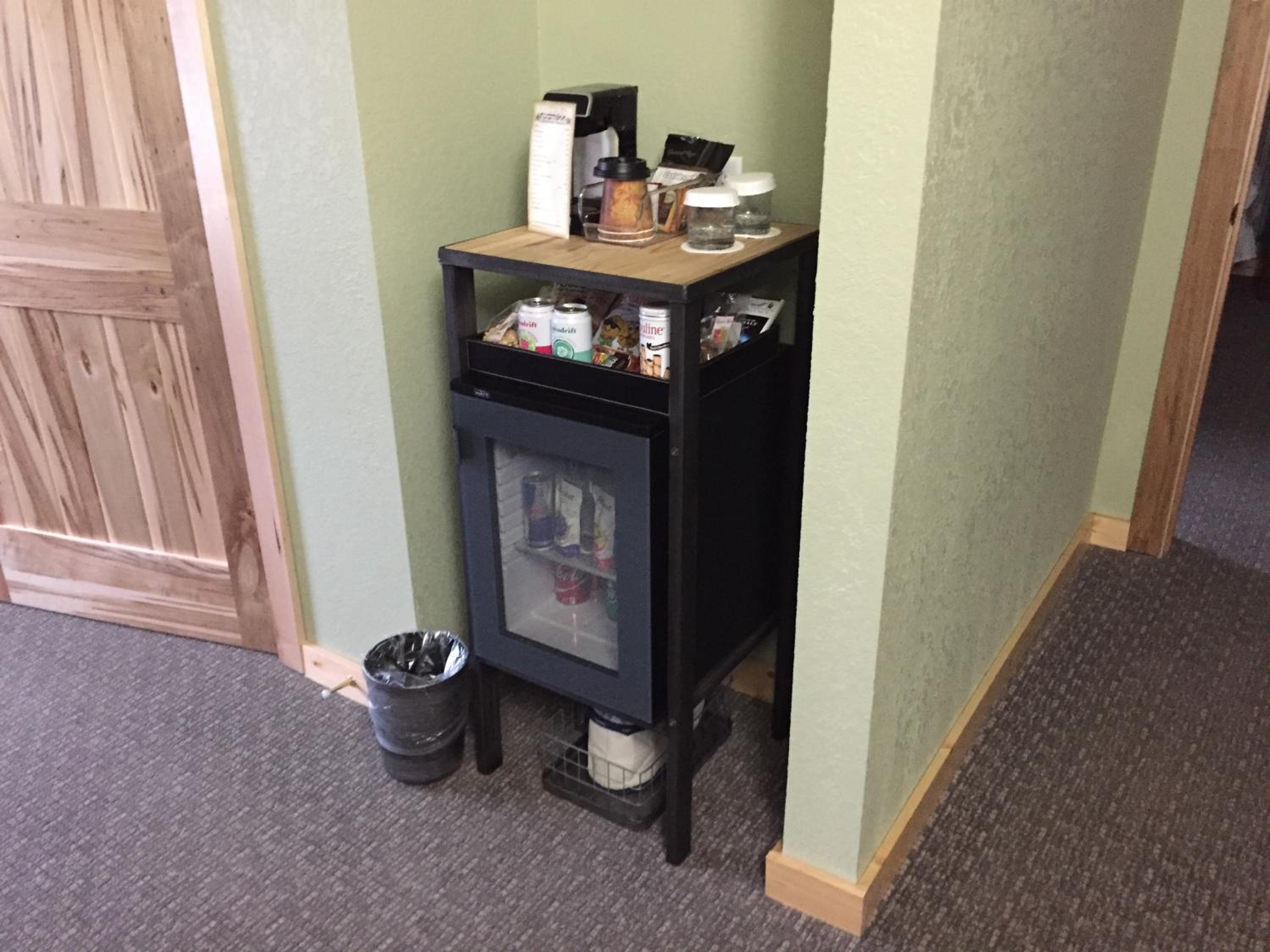 Coffee maker, snacks, and a mini-fridge arranged on a stand inside a hallway alcove.