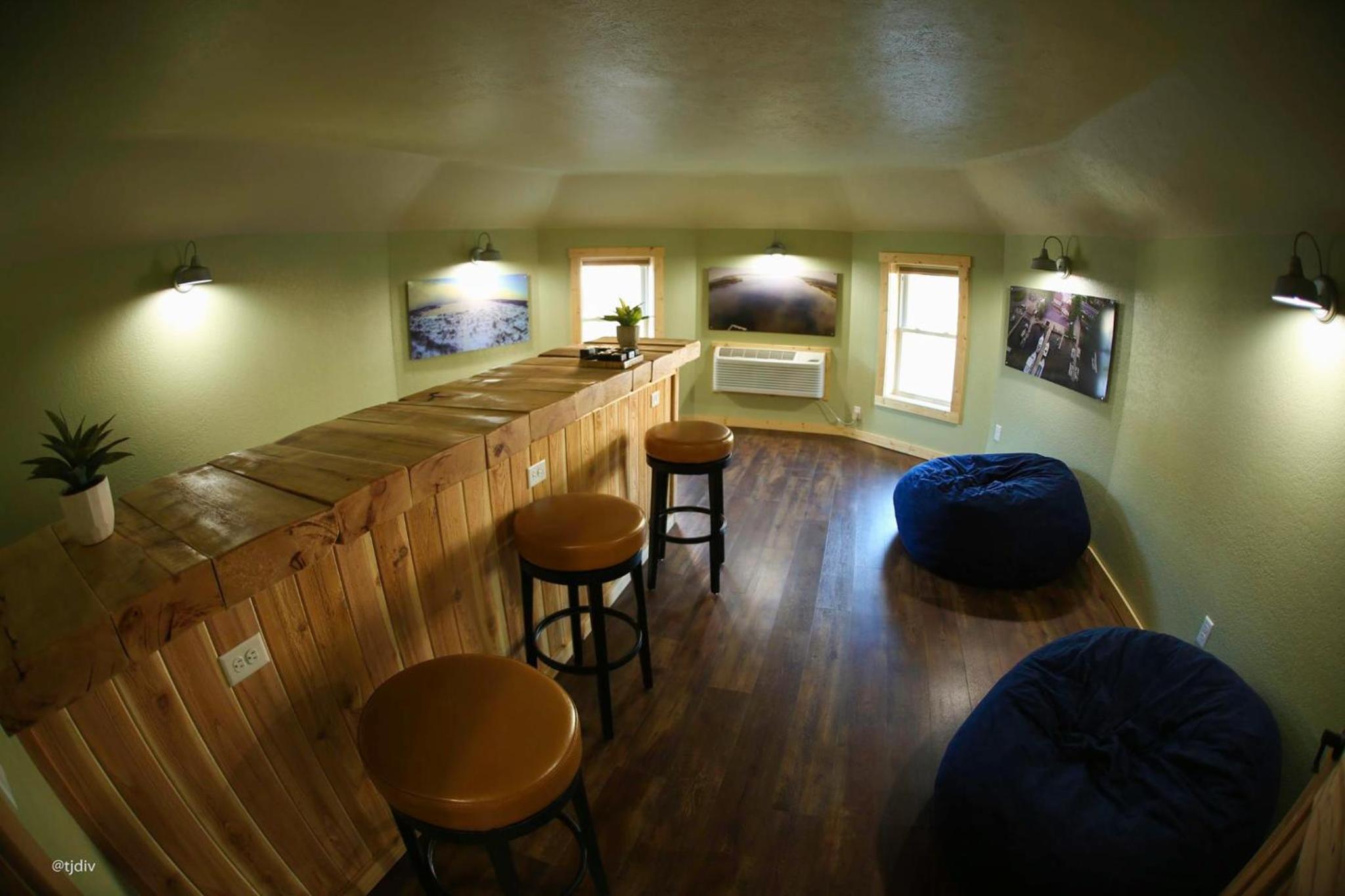 Wood-paneled bar counter with round stools, blue beanbag chairs, and wall art under a sloping ceiling.