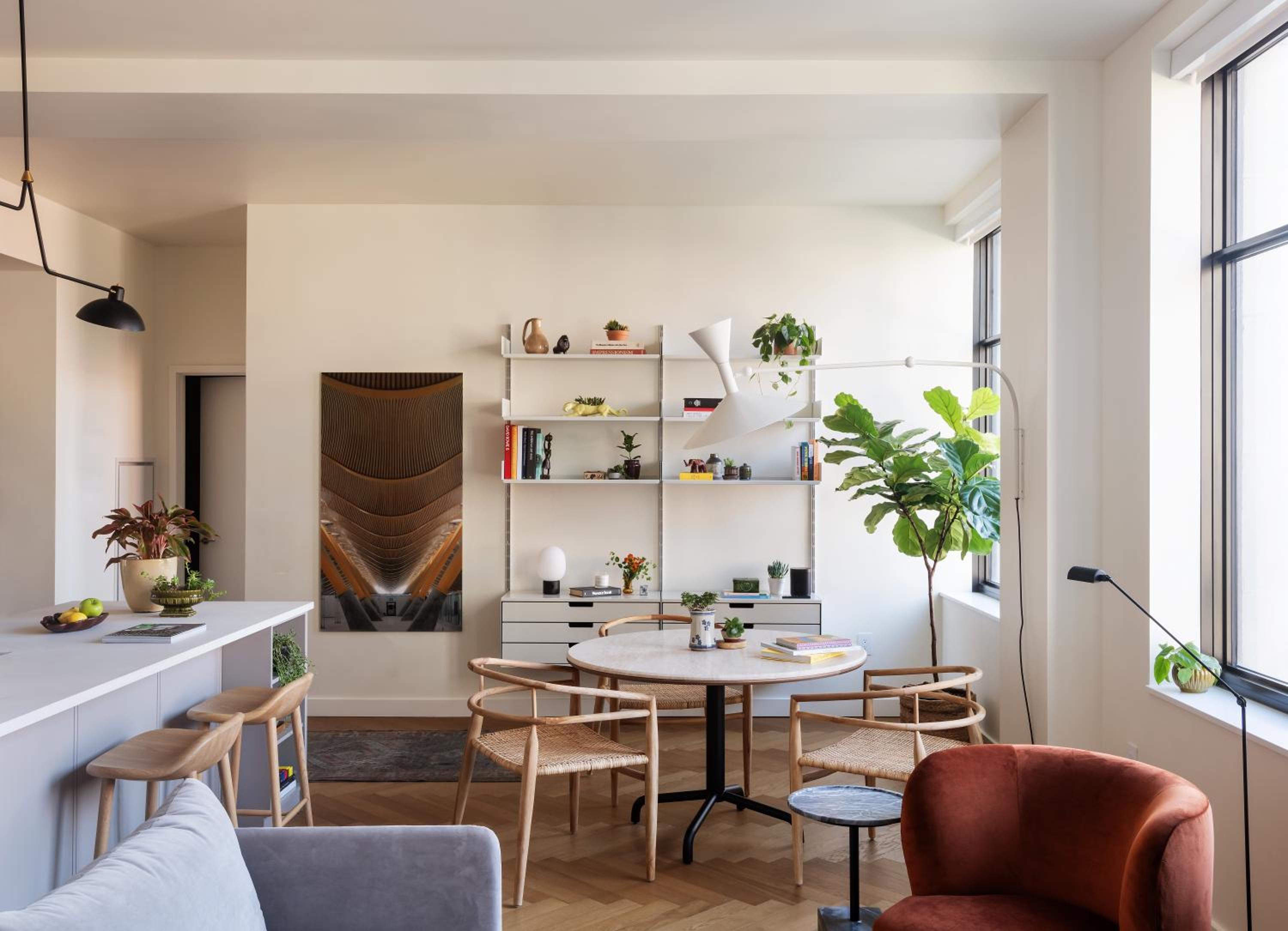 An open-plan living and dining area with parquet floors, a round table with woven chairs, and modular wall shelving.