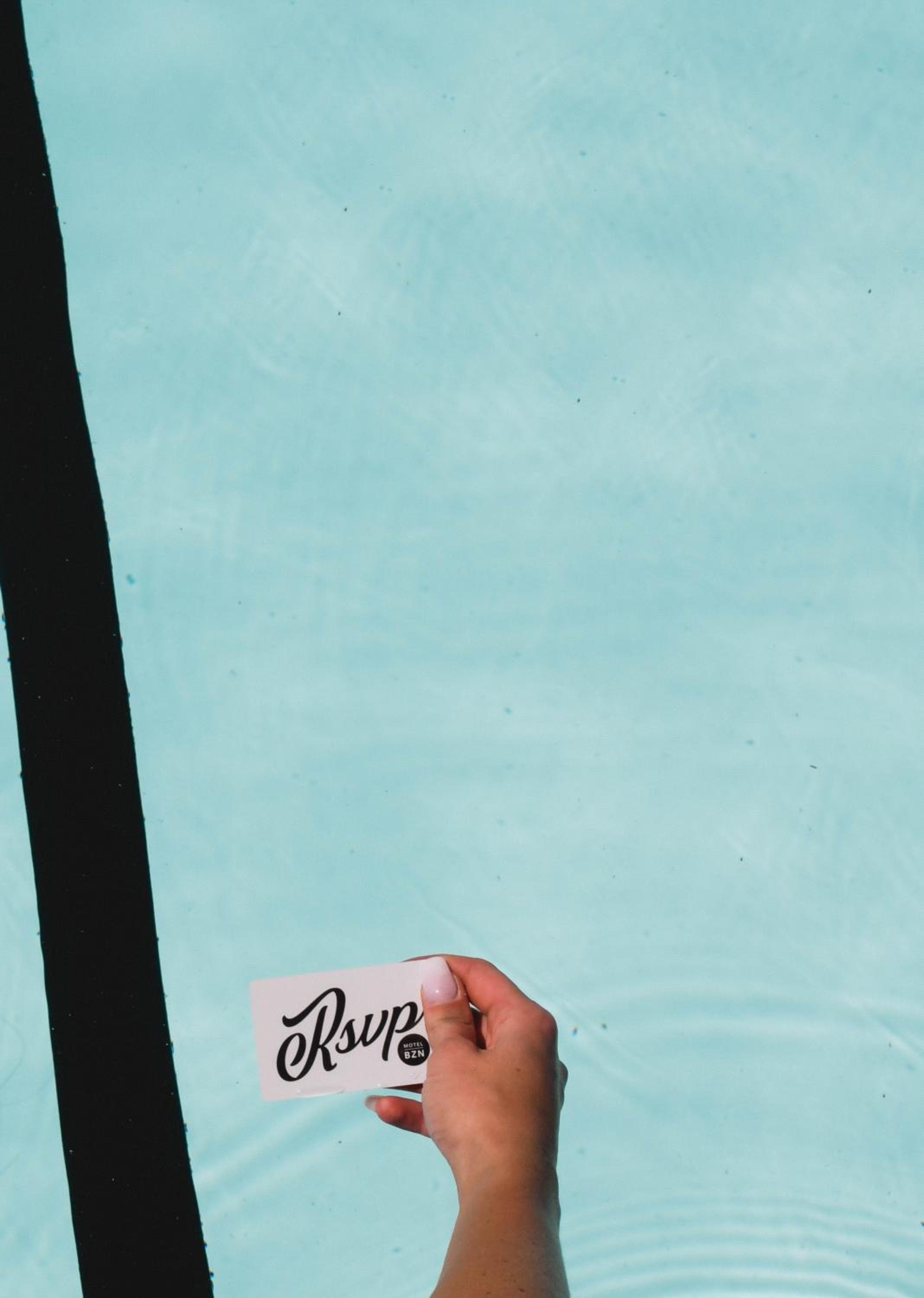 A hand holds a keycard over the pale blue water of a swimming pool.