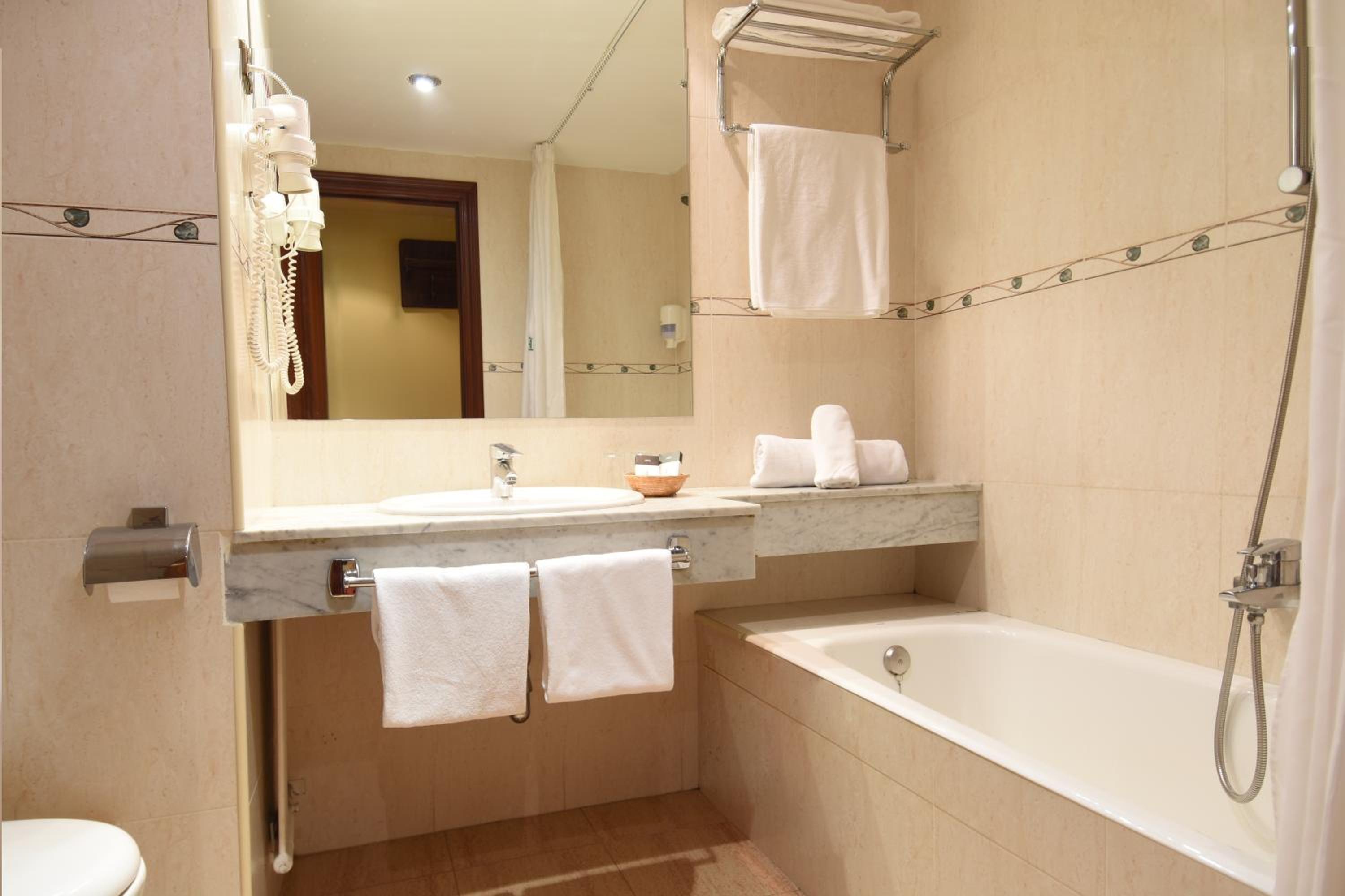 Hotel bathroom featuring a marble vanity counter, a bathtub with shower head, and folded white towels.