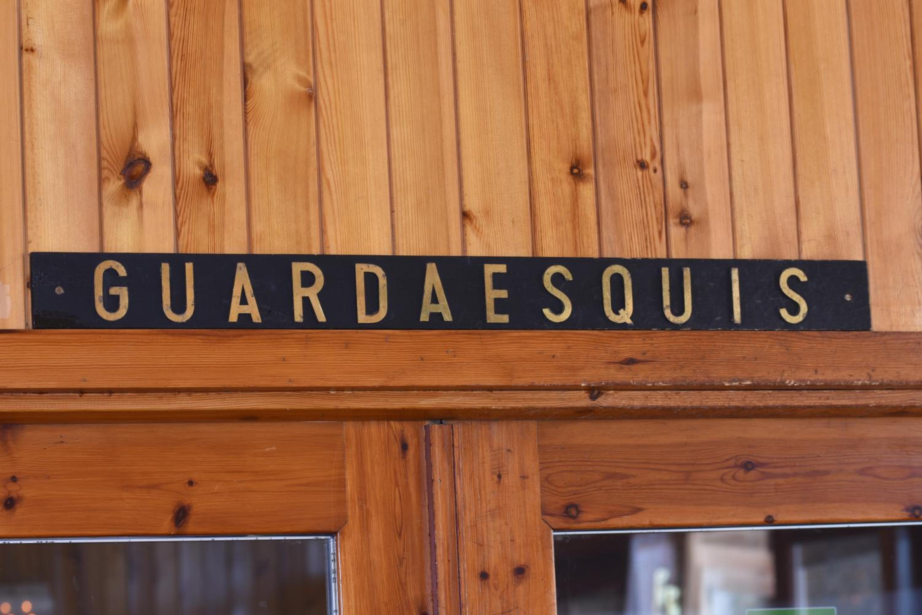 Black sign reading GUARDAESQUIS mounted on a paneled wood wall above a doorway.