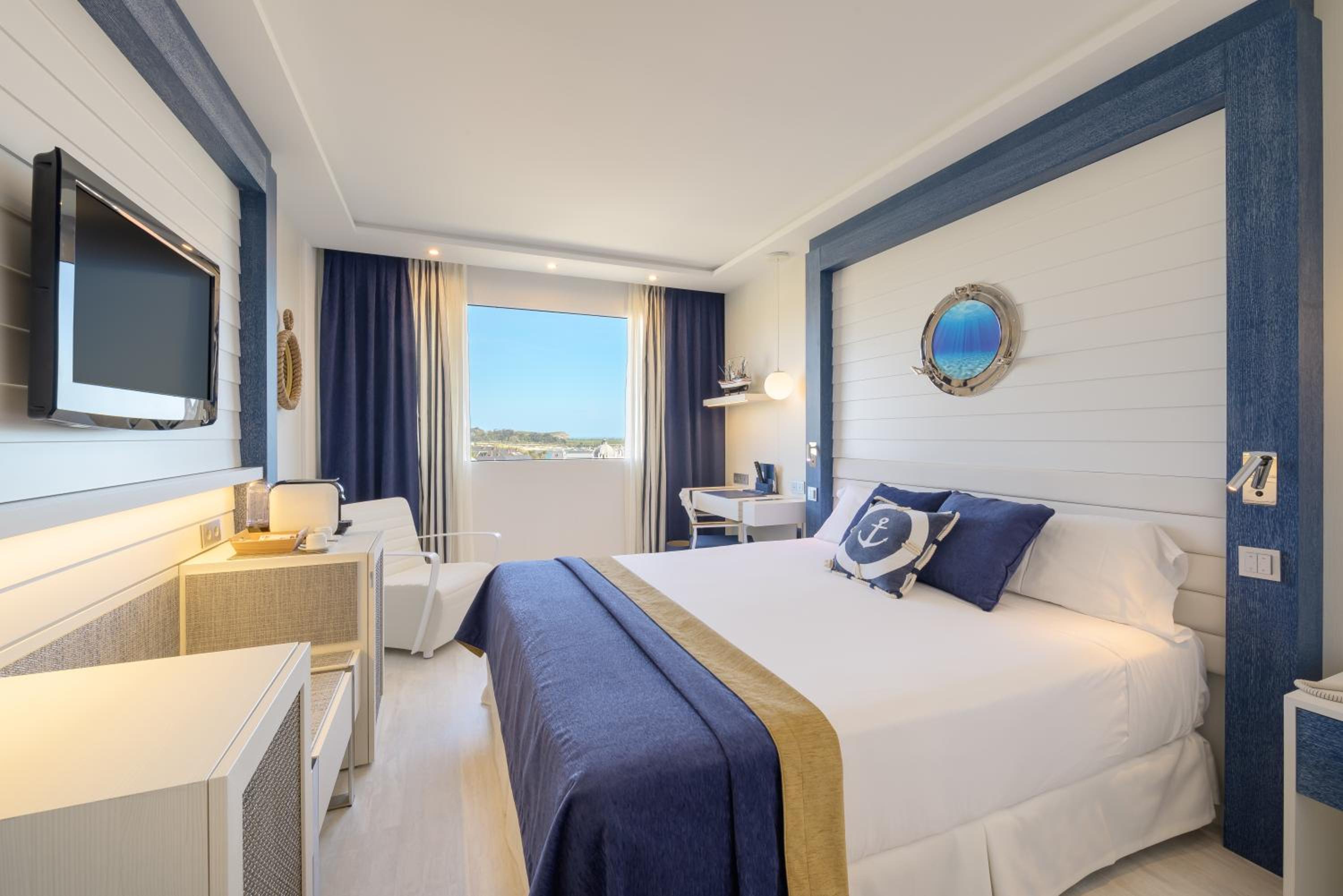 A bright hotel bedroom decorated in white and navy blue, featuring wood-paneled walls and a porthole wall accent.